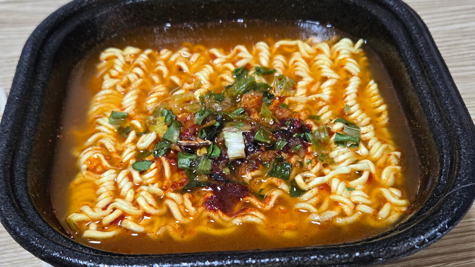 ມີ້ເຜັດເກົາຫຼີ ທຶມແຊລາມຽນ ປາລເກທັອກ ສຳເລັດຮູບ - ນ້ຳແກງສີແດງເຂັ້ມ ເສັ້ນມີ້ຫຍັກ ມີຜັກບົ່ວແລະຜັກກາດຂຽວຢູ່ເທິງ | 하이제이에스비