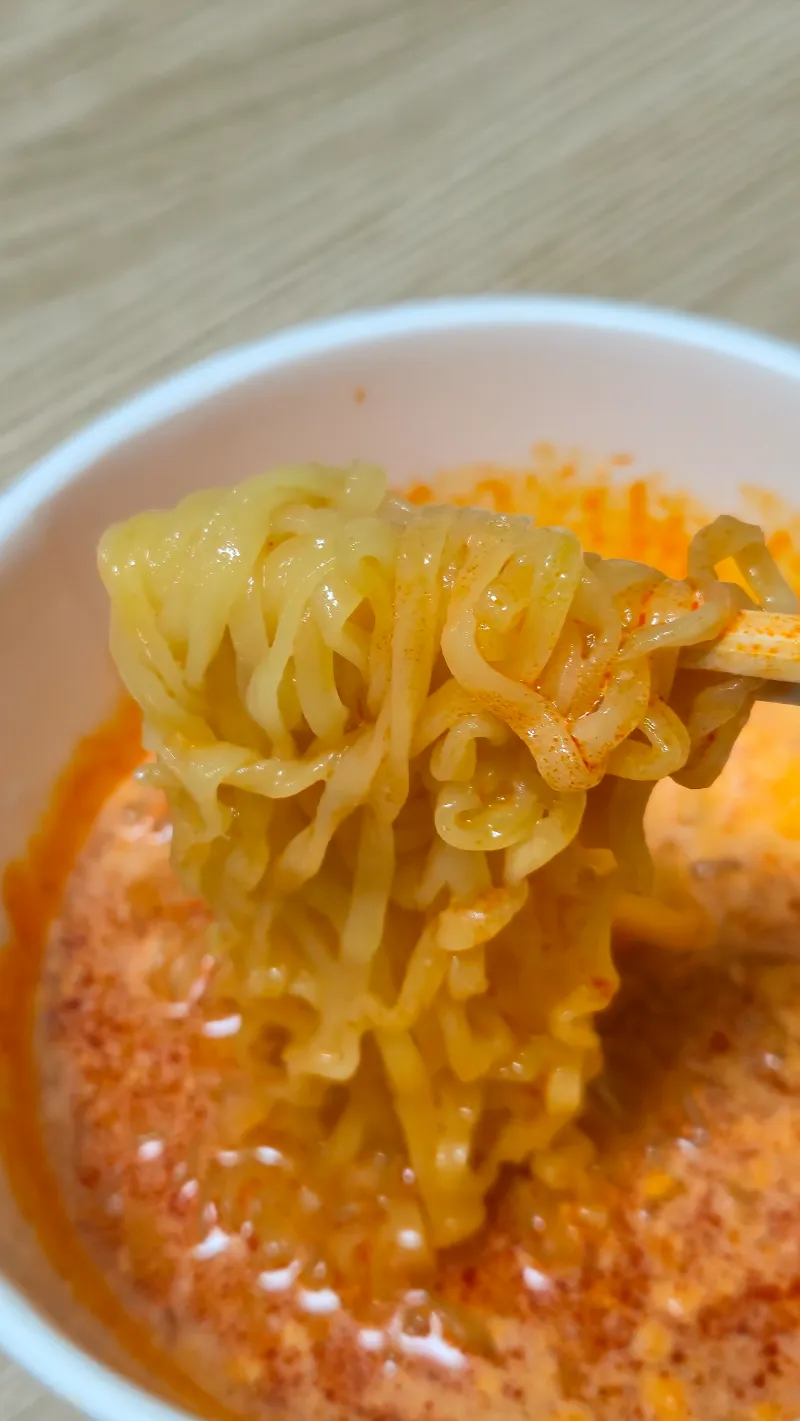 箸で持ち上げたクアトロチーズブルダックの麺（チーズクリームがコーティング） | 하이제이에스비