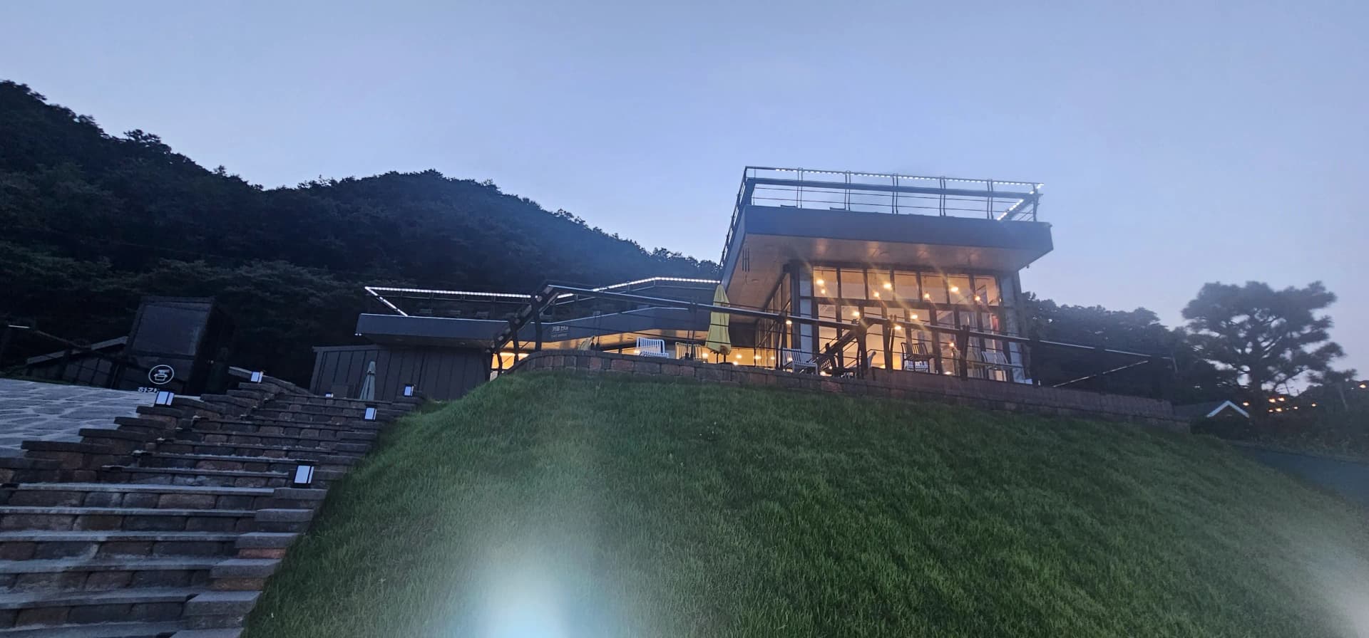 해질녘 카페 반내 외관 — 언덕 위 건물에 조명이 켜지기 시작하는 모습