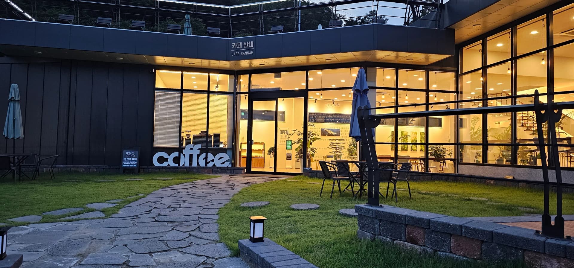 카페 반내 외부 산책로 — 잔디밭 위 조명과 나무