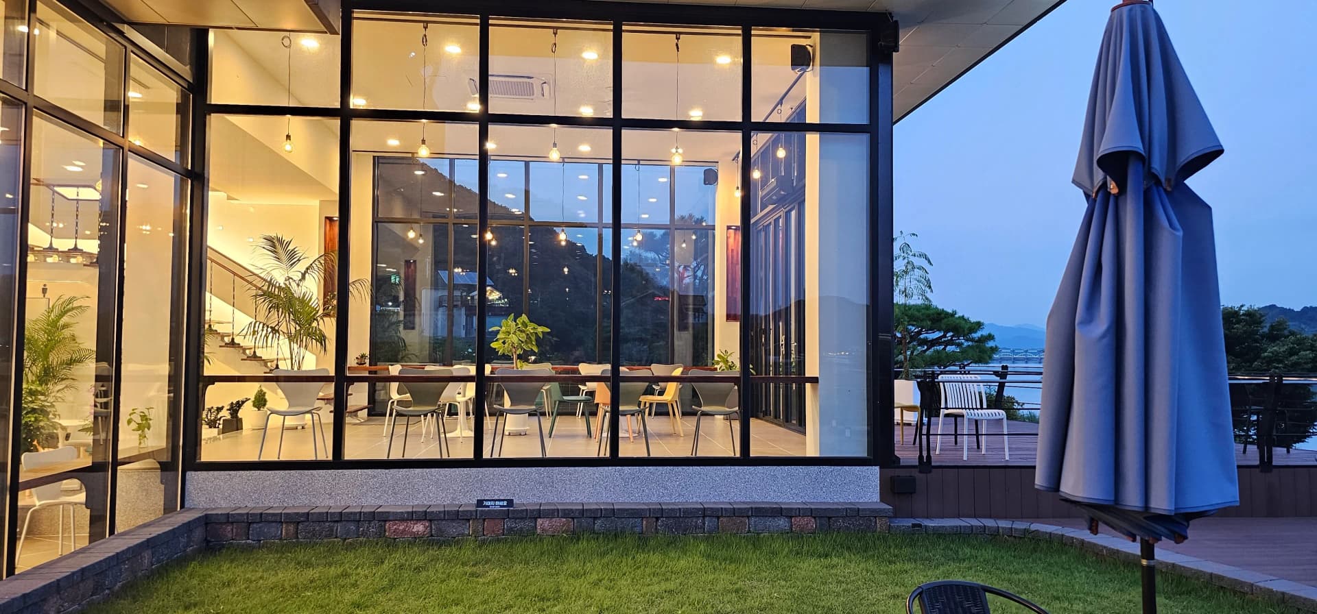 밖에서 바라본 카페 반내 — 전면 유리 너머로 내부 조명, 식물, 컬러풀한 의자가 보이는 야경