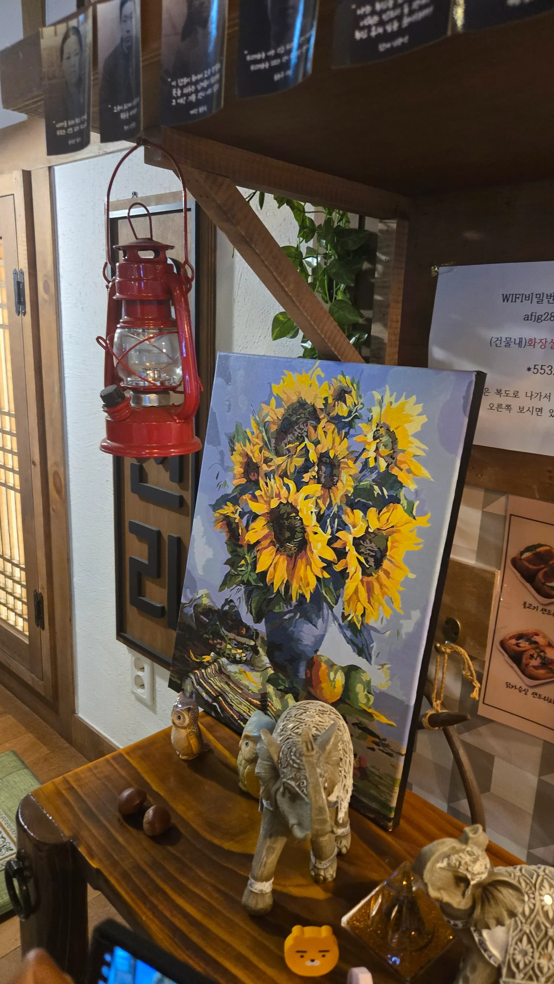 읍천리382 벽면 빨간 등유 랜턴과 해바라기 그림 — 나무 문살 뒤 옛날 사진이 걸린 복고풍 장식 | 하이제이에스비