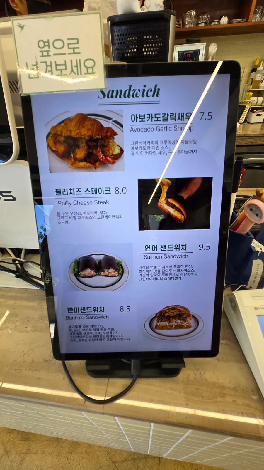 Green Bakery counter screen showing sandwich menu with prices