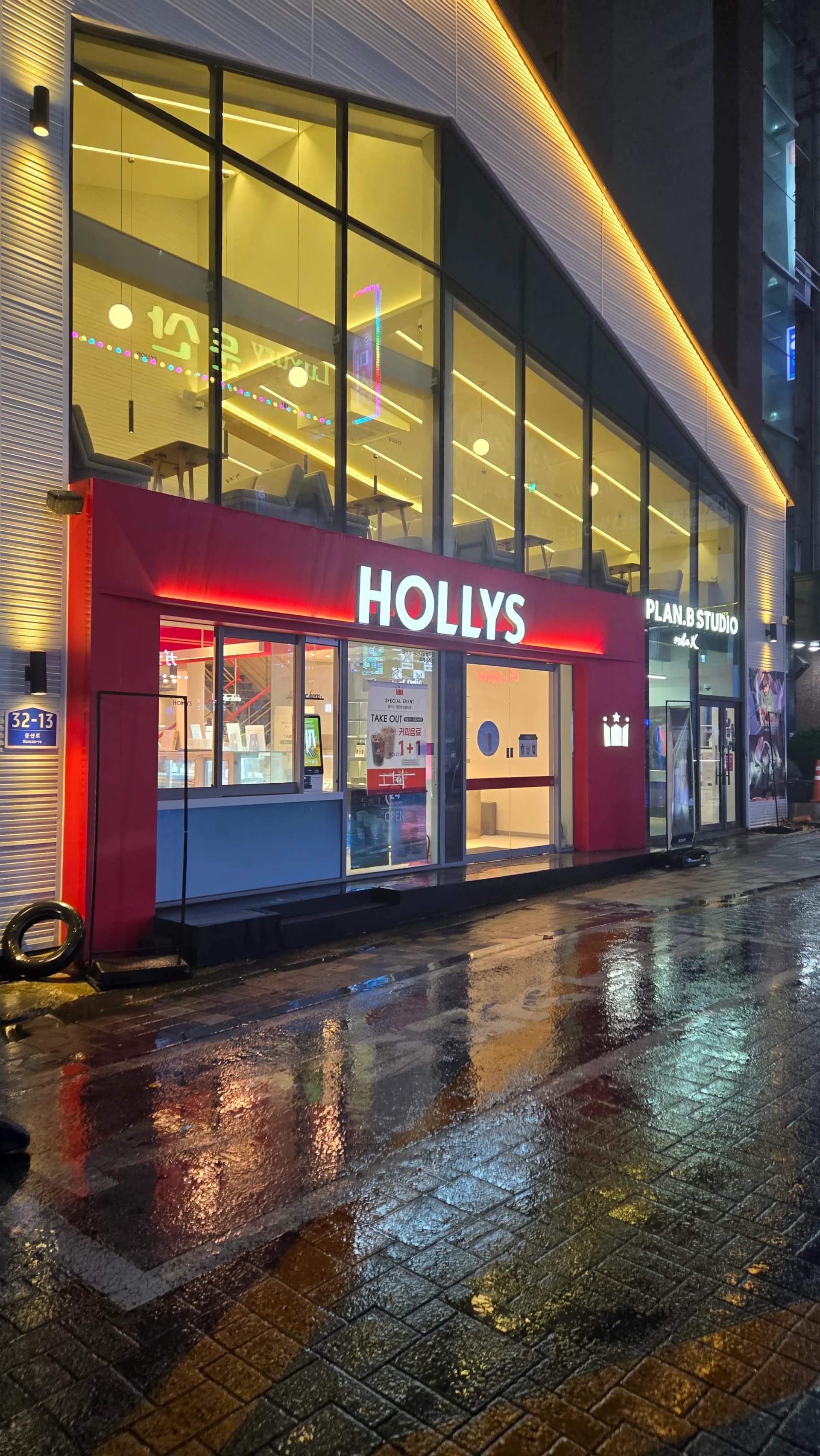 비 오는 새벽 거리에서 환하게 불빛이 켜져 있는 할리스 커피 매장 외관