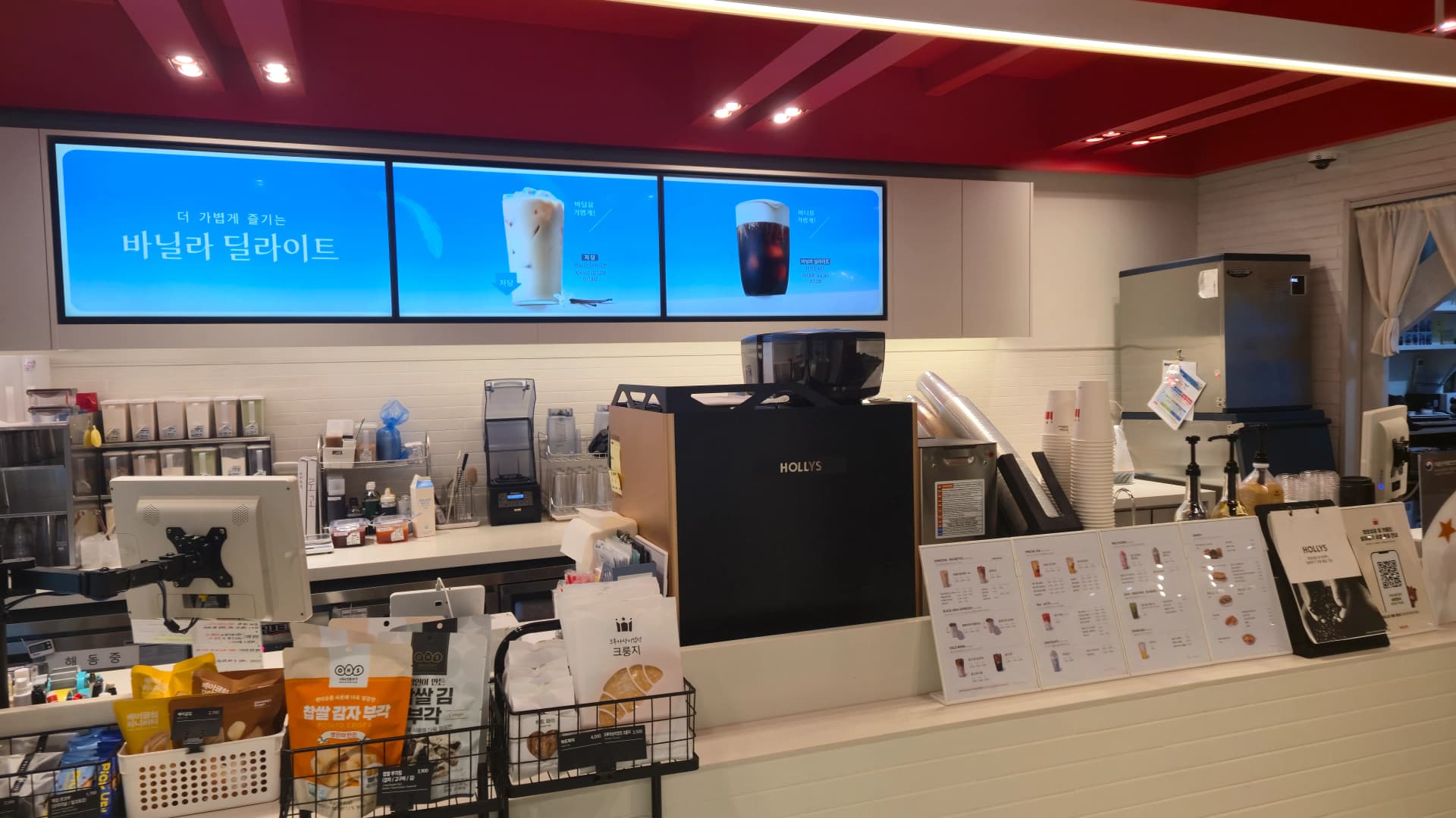 할리스 커피 카운터 근접 촬영으로 커피 머신과 바닐라 딜라이트 광고 화면이 보인다