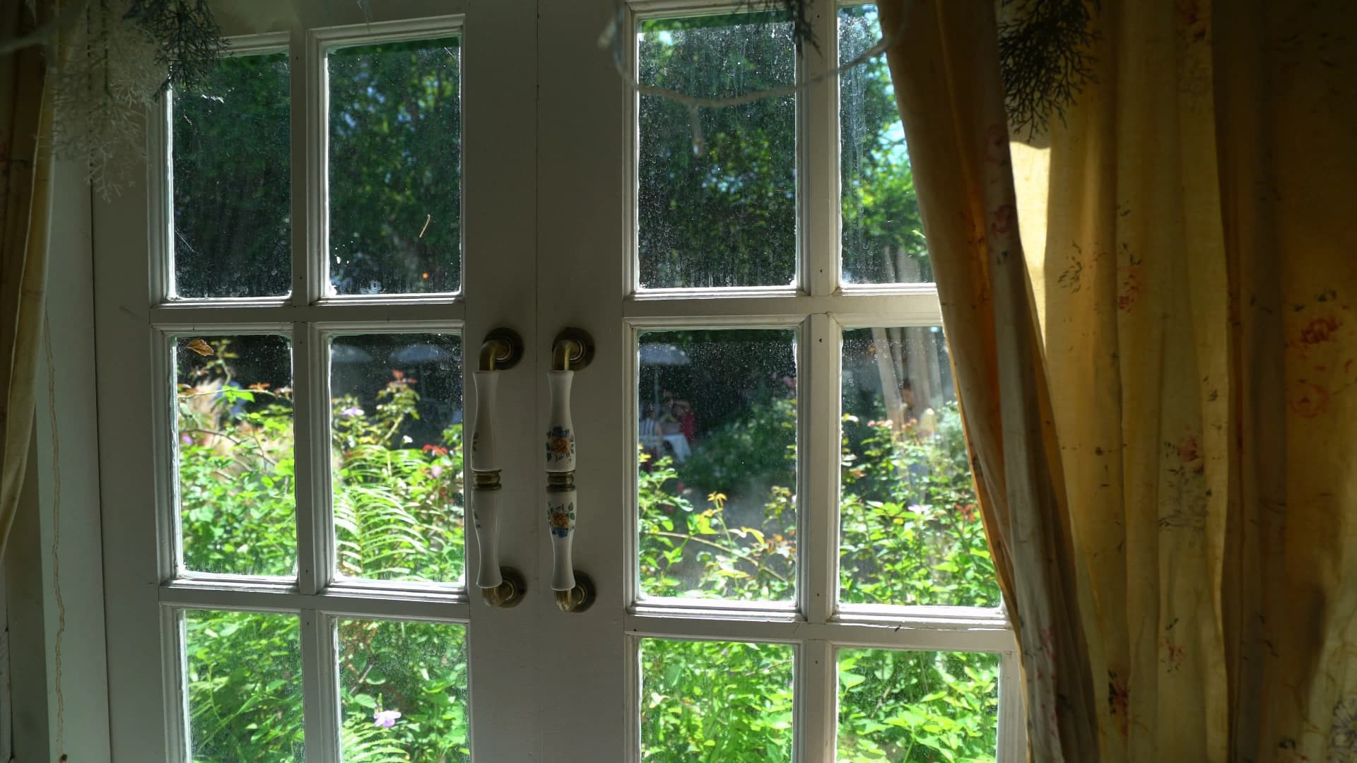 Hand-painted ceramic door handle beside floral curtain with garden greenery through the window