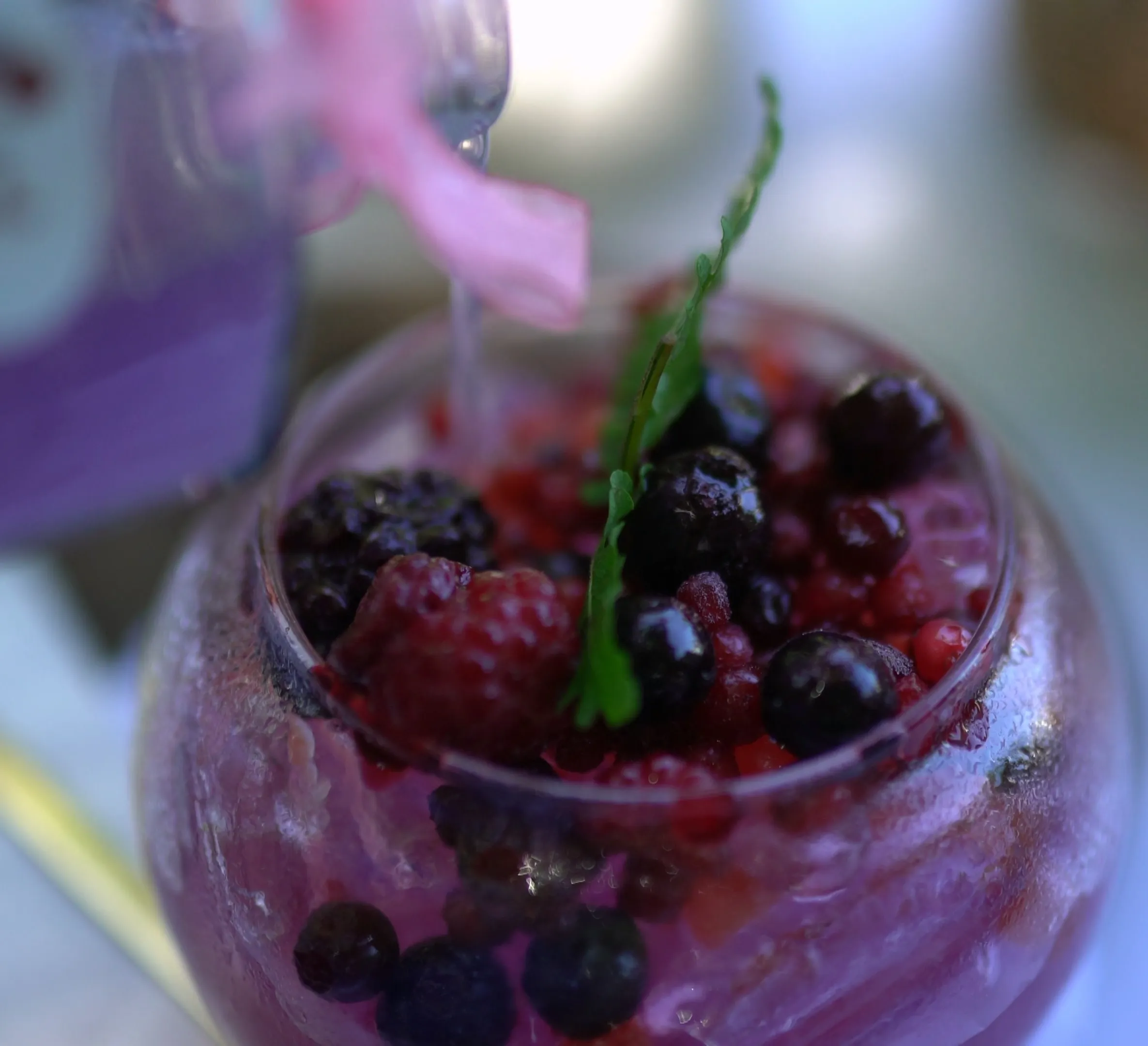 Purple syrup being slowly poured over berries and ice into a glass
