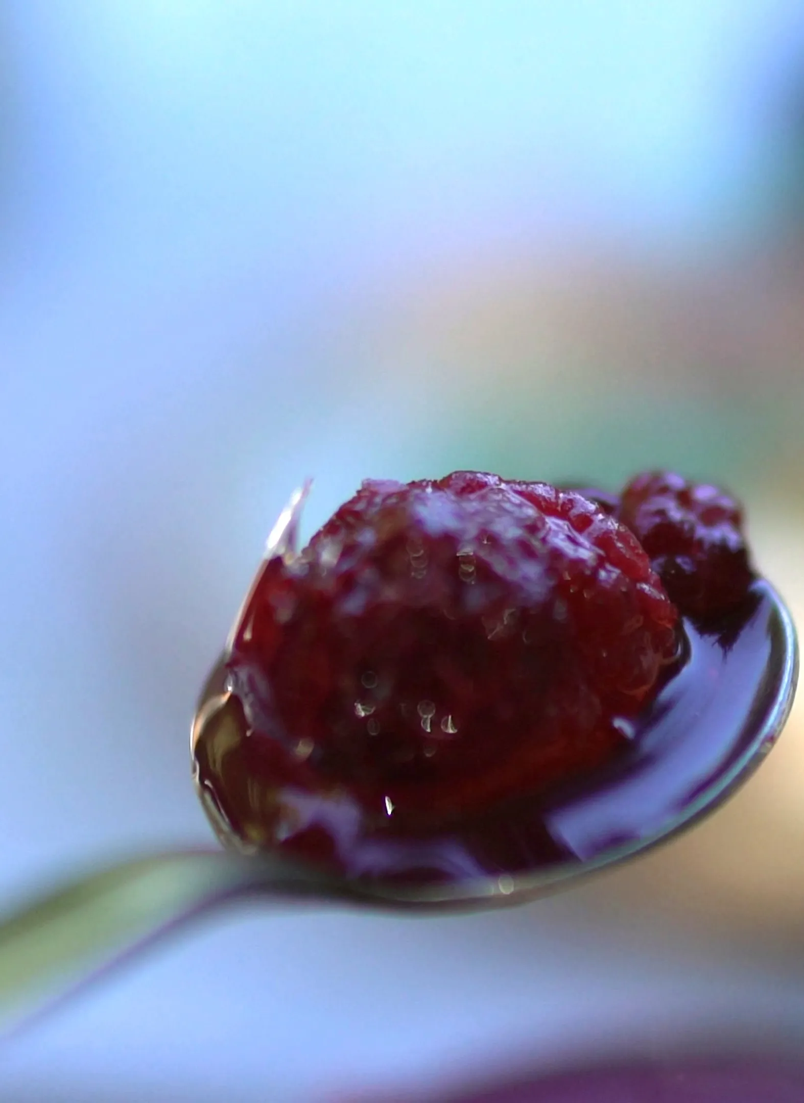 Spoon lifting a single raspberry with purple syrup dripping off in close-up