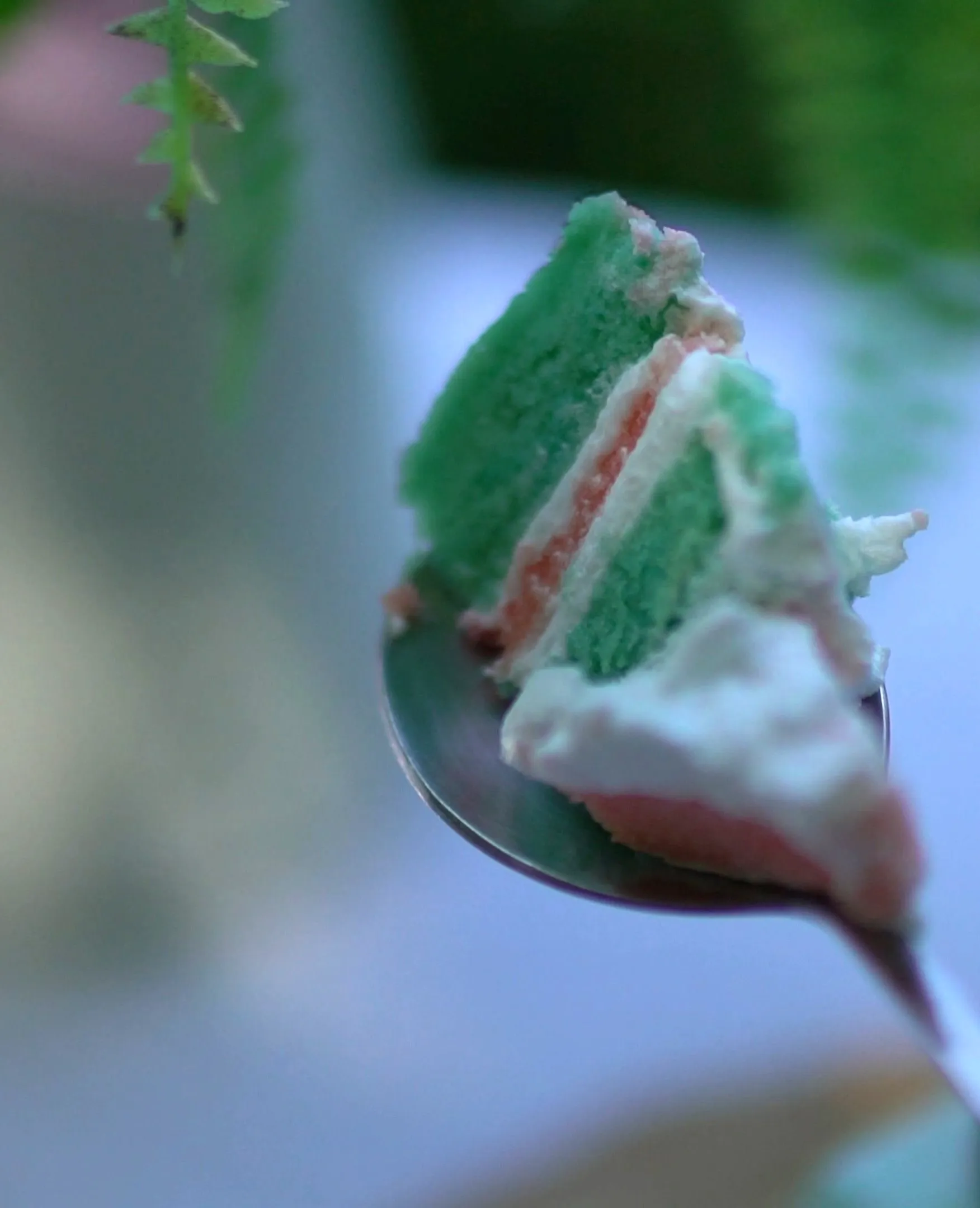 Single forkful of three-layer cake held up with blurred garden in the background
