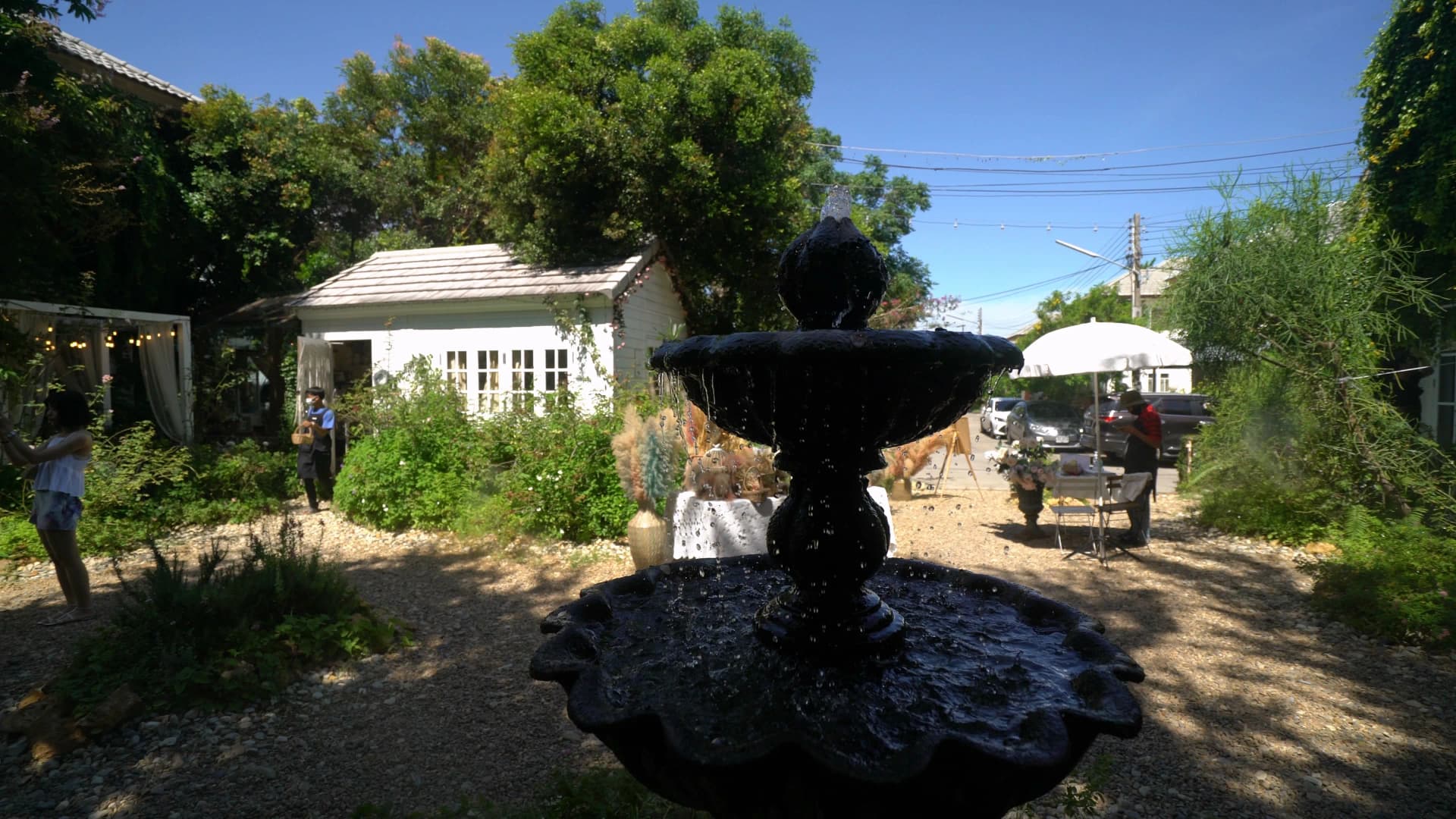 Black fountain in the centre of Pa Dee in the Wild garden with white cottage and fairy lights behind