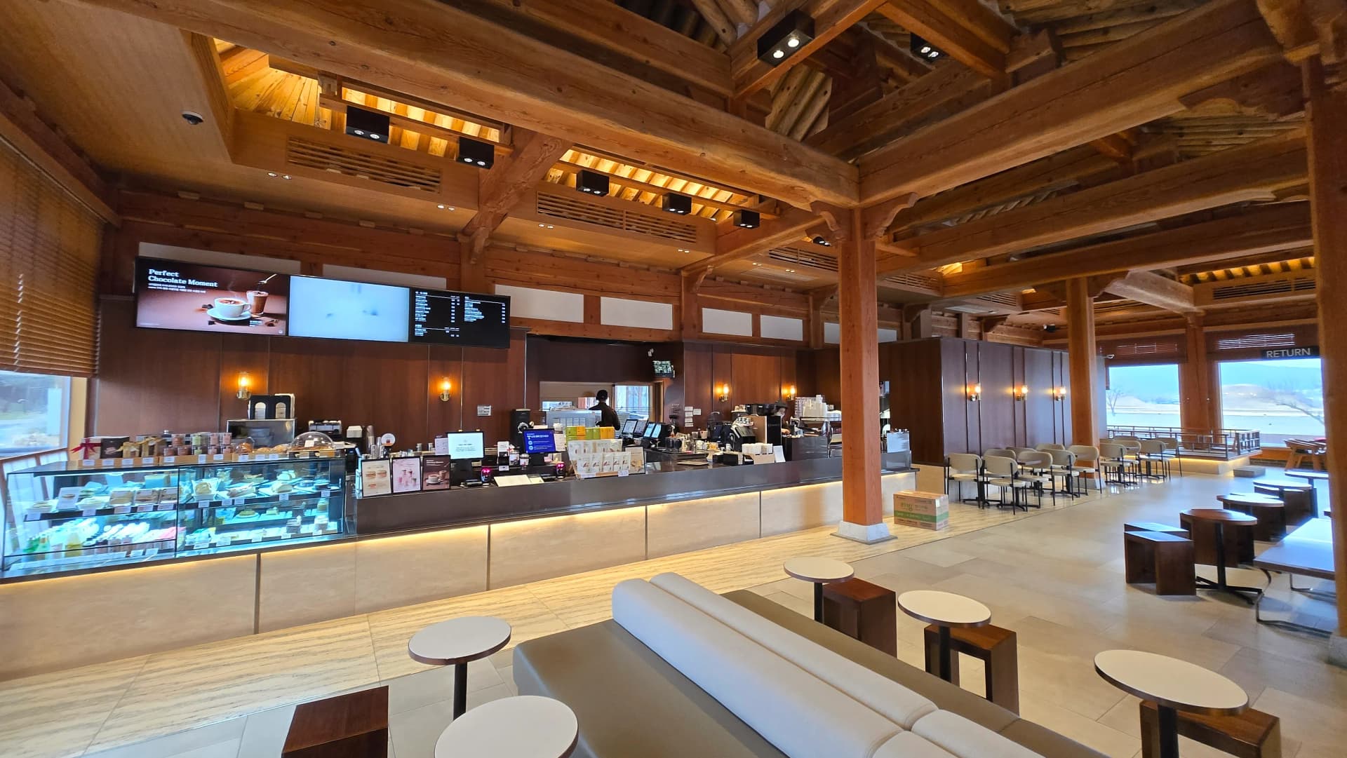 Toàn cảnh bên trong Paul Bassett Gyeongju từ cửa vào — xà gỗ lớn và rui mè trong sảnh rộng | 하이제이에스비