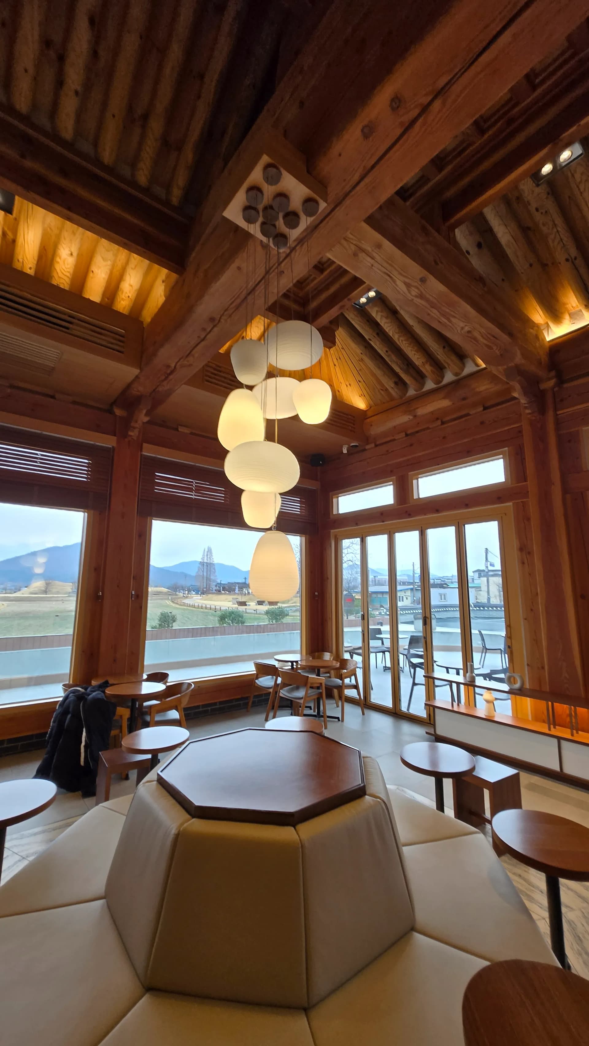 Khu ngồi bệt Paul Bassett Gyeongju — bàn gỗ thấp, đệm ngồi, tường trắng hanok và khung cửa gỗ | 하이제이에스비