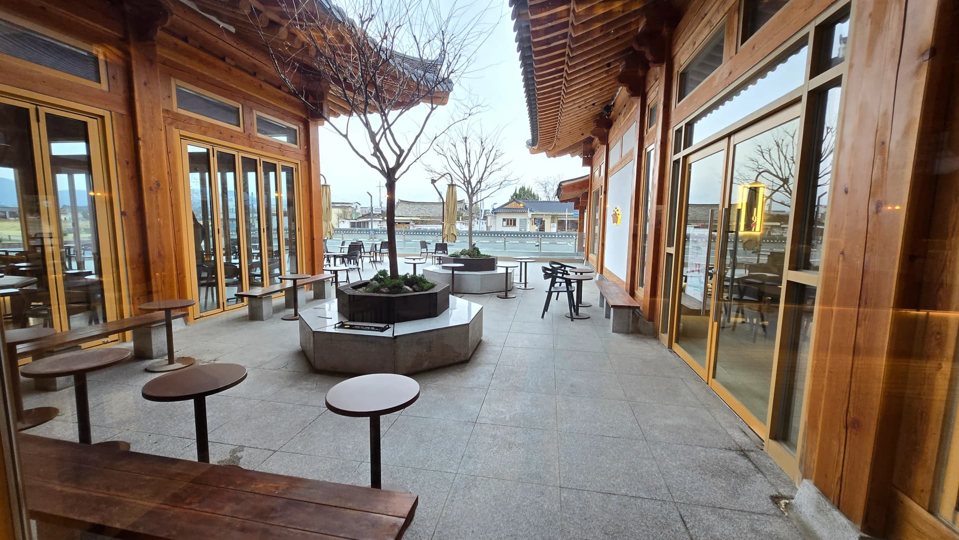 Ghế hành lang ngoài trời Paul Bassett Gyeongju — bồn hoa bát giác và cây xanh dưới mái hiên hanok | 하이제이에스비