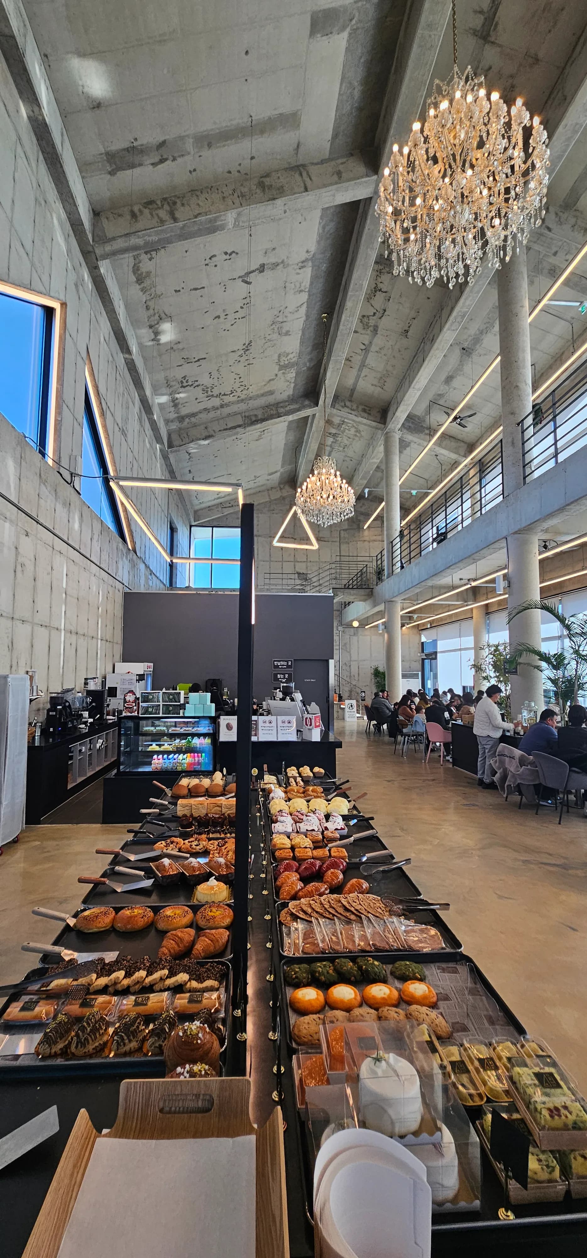 Muonekano wa ndani wa Semo Cafe, dari refu, taa za kuning'inia na sehemu ya kuonyesha mikate | 하이제이에스비