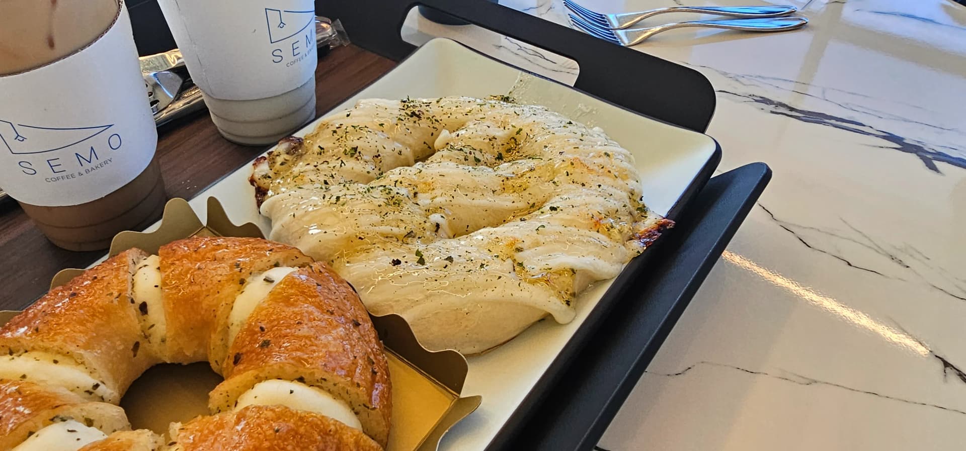 Mpangilio wa mikate na vinywaji katika Semo Cafe kwenye meza ya marumaru huku mwanga wa jua ukiingia | 하이제이에스비