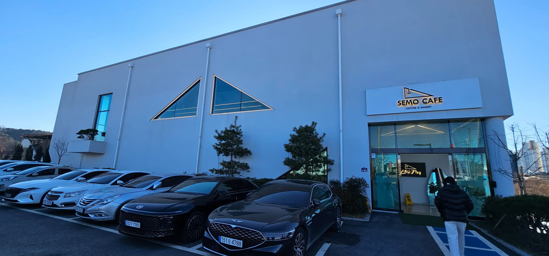 Mwonekano wa nje wa Semo Cafe, jengo jeupe lenye madirisha ya umbo la pembe tatu karibu na Ziwa Daecheong | 하이제이에스비