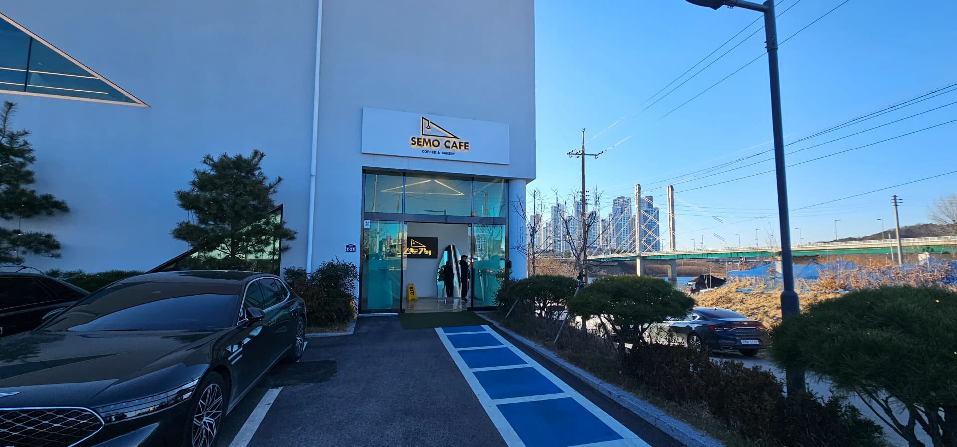 Lango la kuingia la SEMO CAFE lenye bango na mandhari ya Daraja la Daecheong kwa mbali | 하이제이에스비