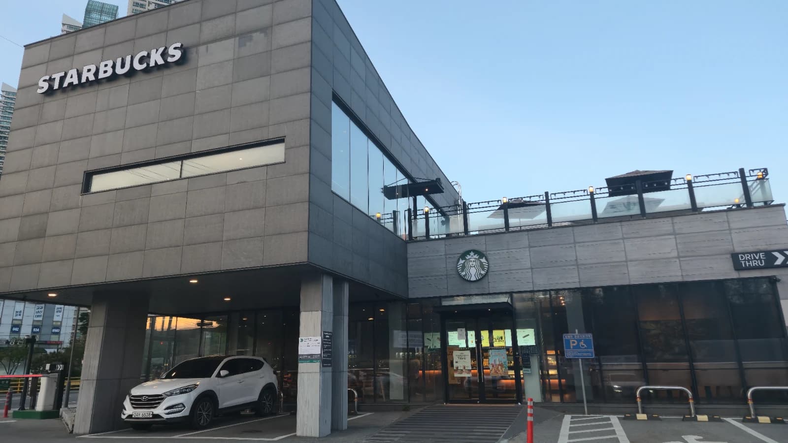 Fachada de uma loja Starbucks drive-thru na Coreia do Sul à noite, com estacionamento e prédio completo
