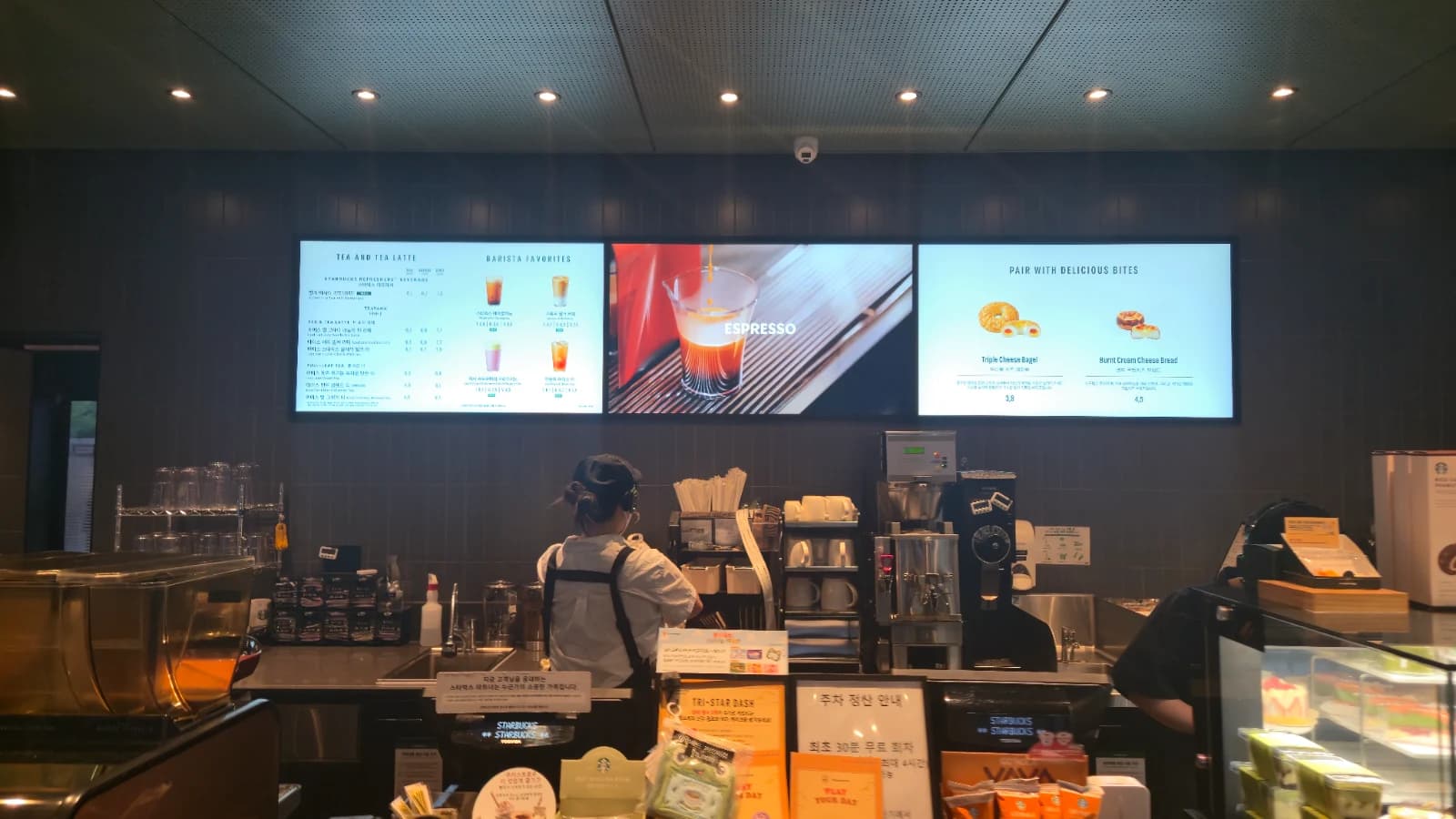 Balcão de um Starbucks coreano com três painéis digitais de menu e atendente com headset