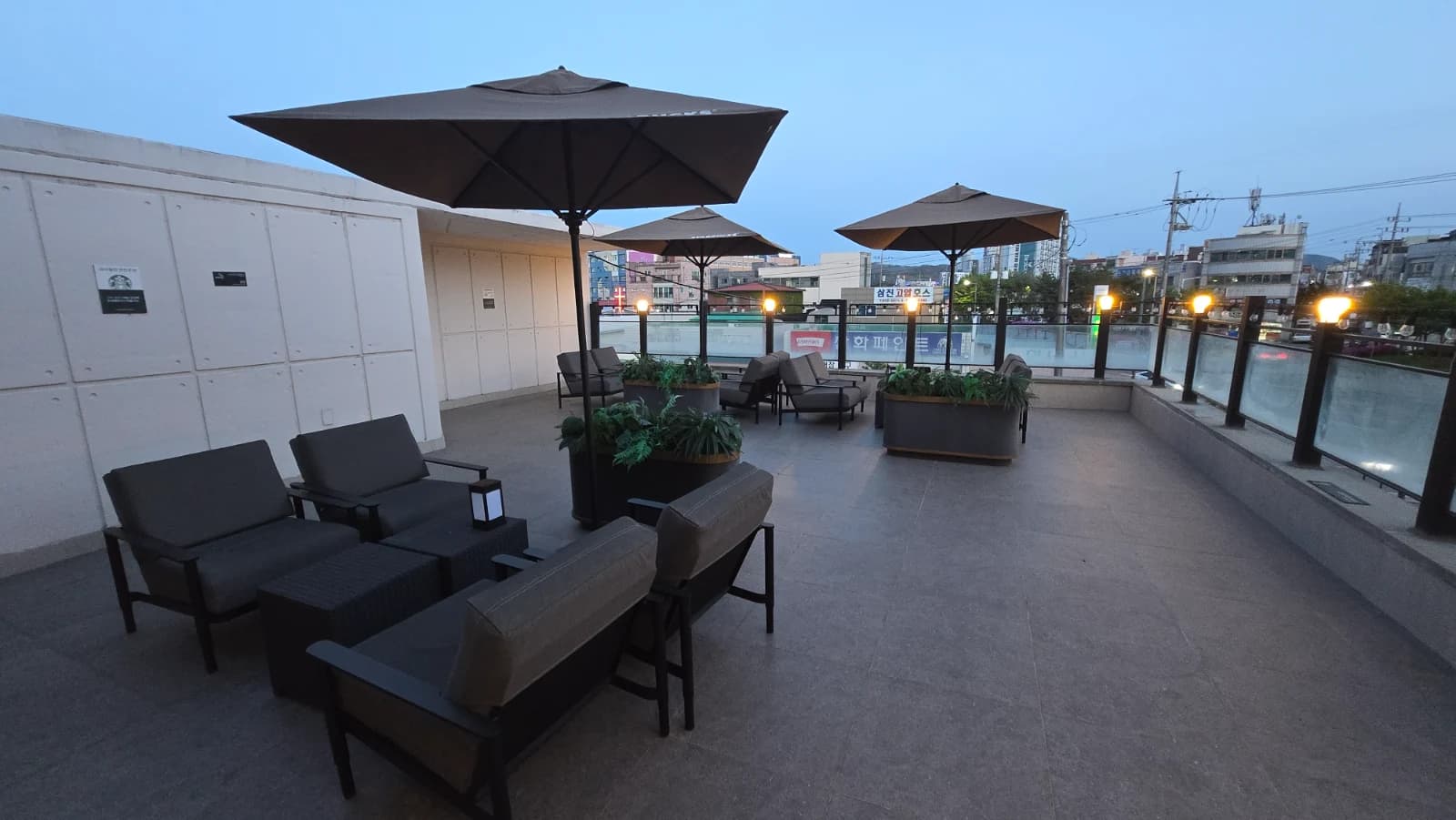 Terraço ao ar livre no segundo andar do Starbucks coreano com guarda-sol, sofás e céu do entardecer