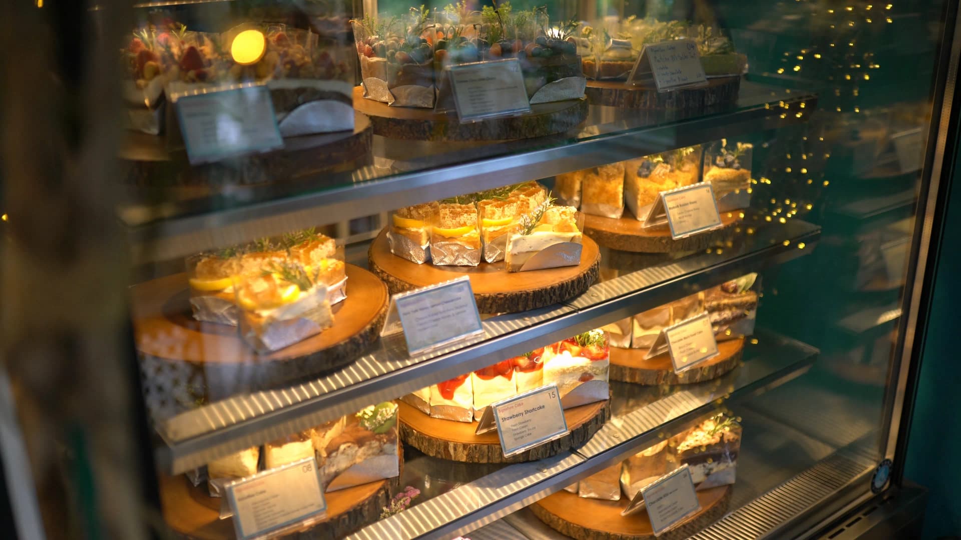 Close-up of cake slices displayed on wooden rounds alongside small cactus pots in the bakery showcase