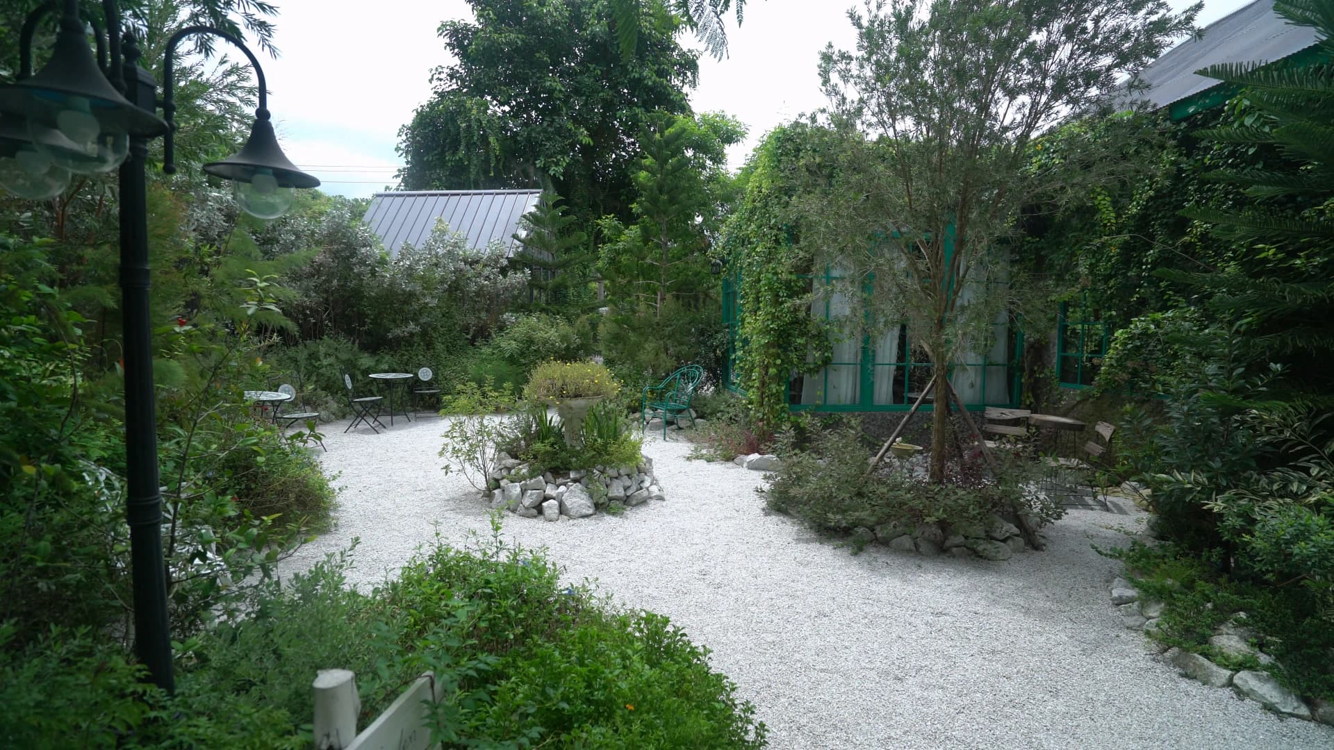 View from the opposite end of the garden showing a vintage street lamp, stone planters, and layered rooflines