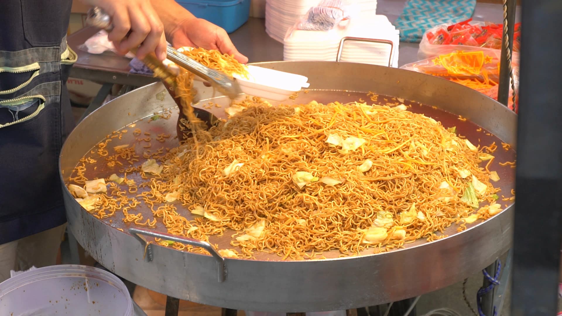 태국 시장 간장 볶음면 – 큰 철판에 수북하게 쌓인 볶음면을 용기에 담아주는 모습