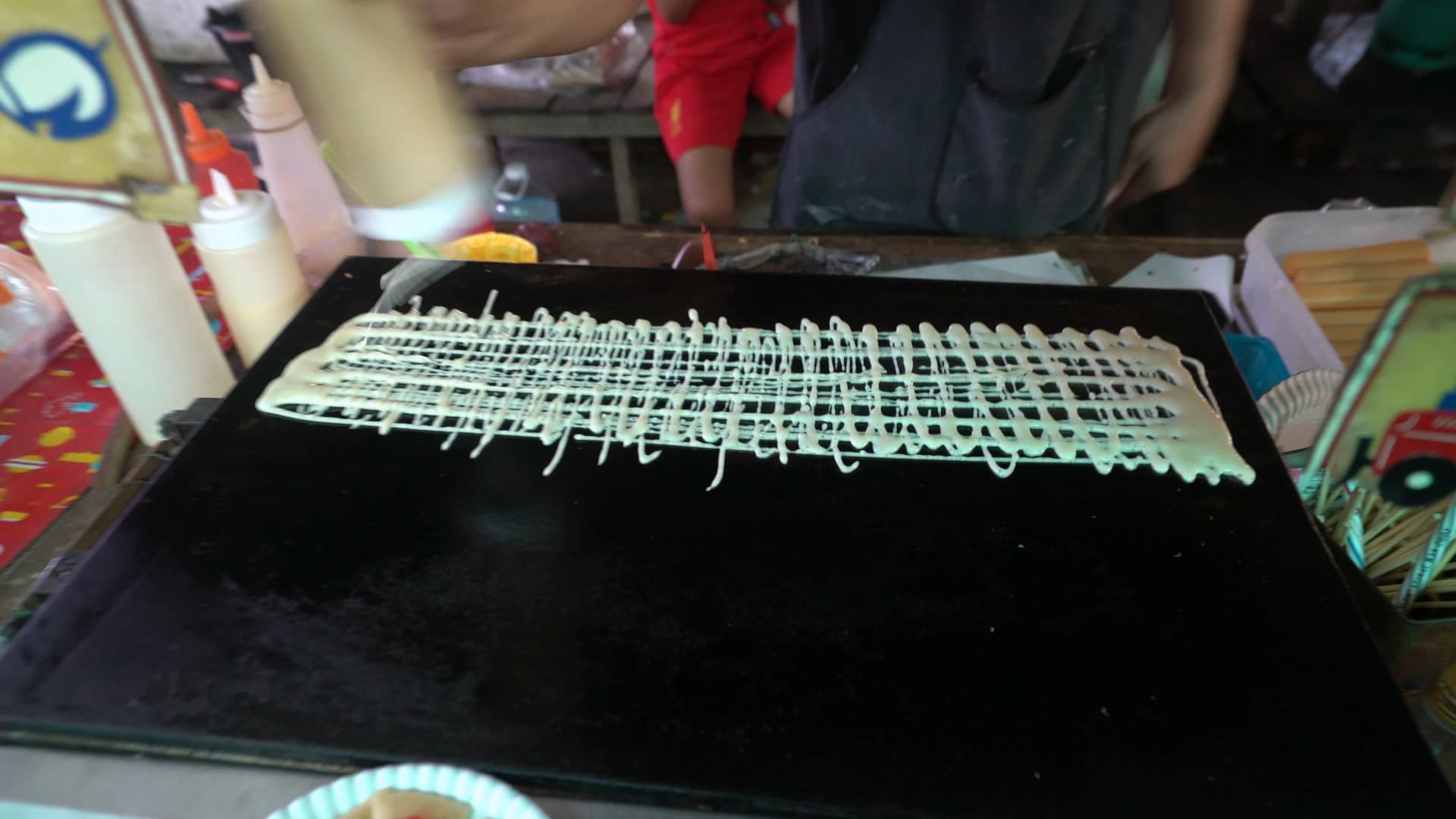 태국 시장 그물 반죽 소시지 꼬치 – 철판 위에 액체 반죽을 격자 모양으로 짜는 모습