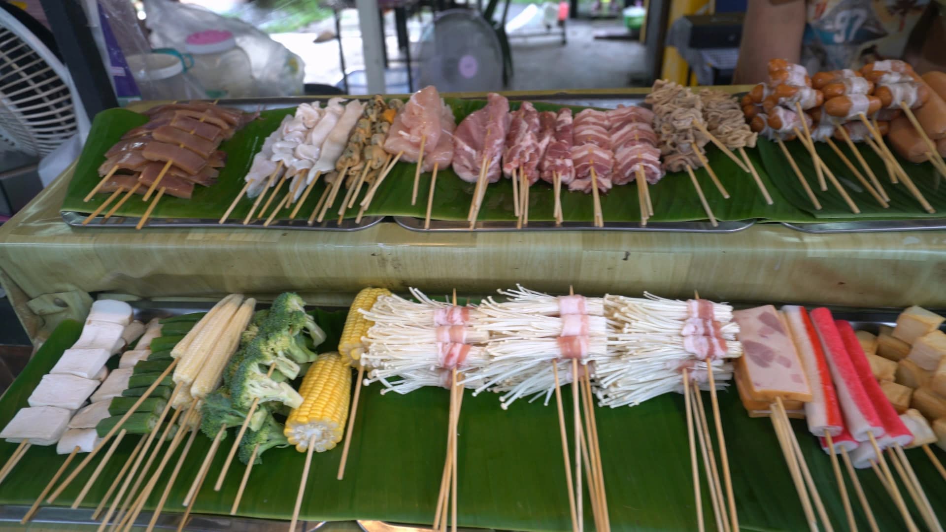 태국 시장 마라꼬치 진열 – 바나나잎 위에 소시지 오징어 돼지고기 두부 브로콜리 옥수수 등 꼬치가 종류별로 깔린 모습