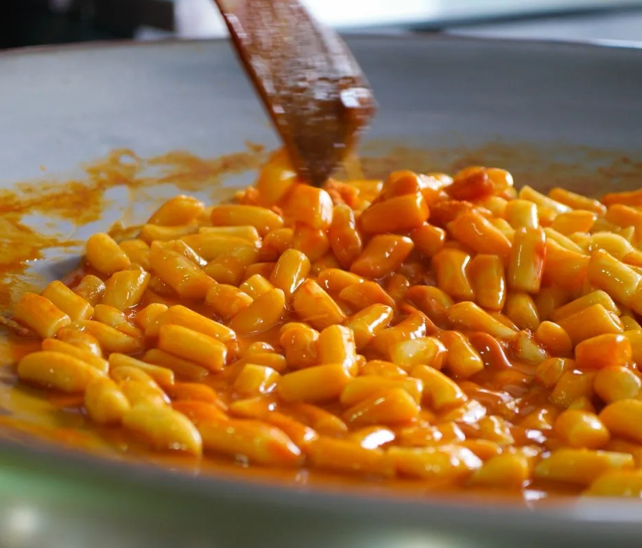 Close-up of glossy tteokbokki soaking in spicy red sauce on iron plate | 하이제이에스비
