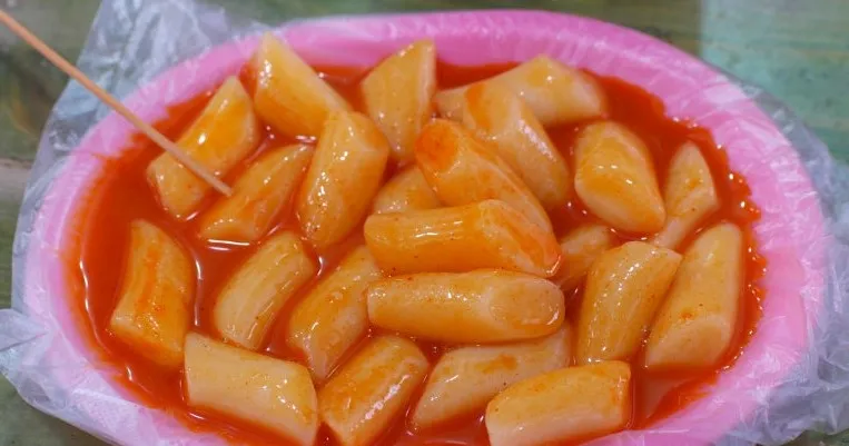 Tteokbokki served on a pink plate with plastic lining and toothpick | 하이제이에스비