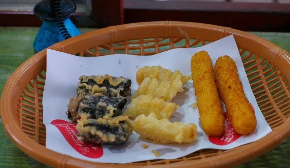 Assorted fried snacks in a basket including gimmari twigim and cheese sticks at a bunsik shop | 하이제이에스비