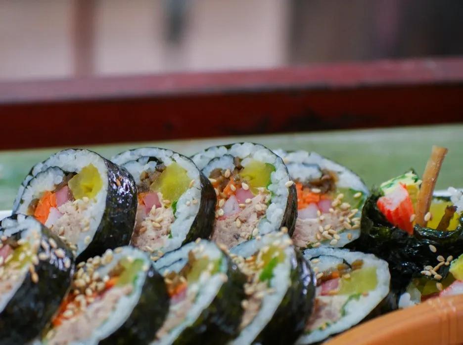 Multiple tuna kimbap pieces lined up showing cross-section layers of ingredients | 하이제이에스비