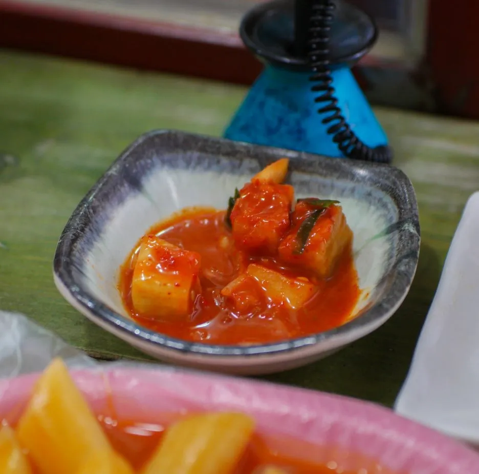Red cubed radish kimchi kkakdugi served in a small ceramic bowl as a bunsik side dish | 하이제이에스비