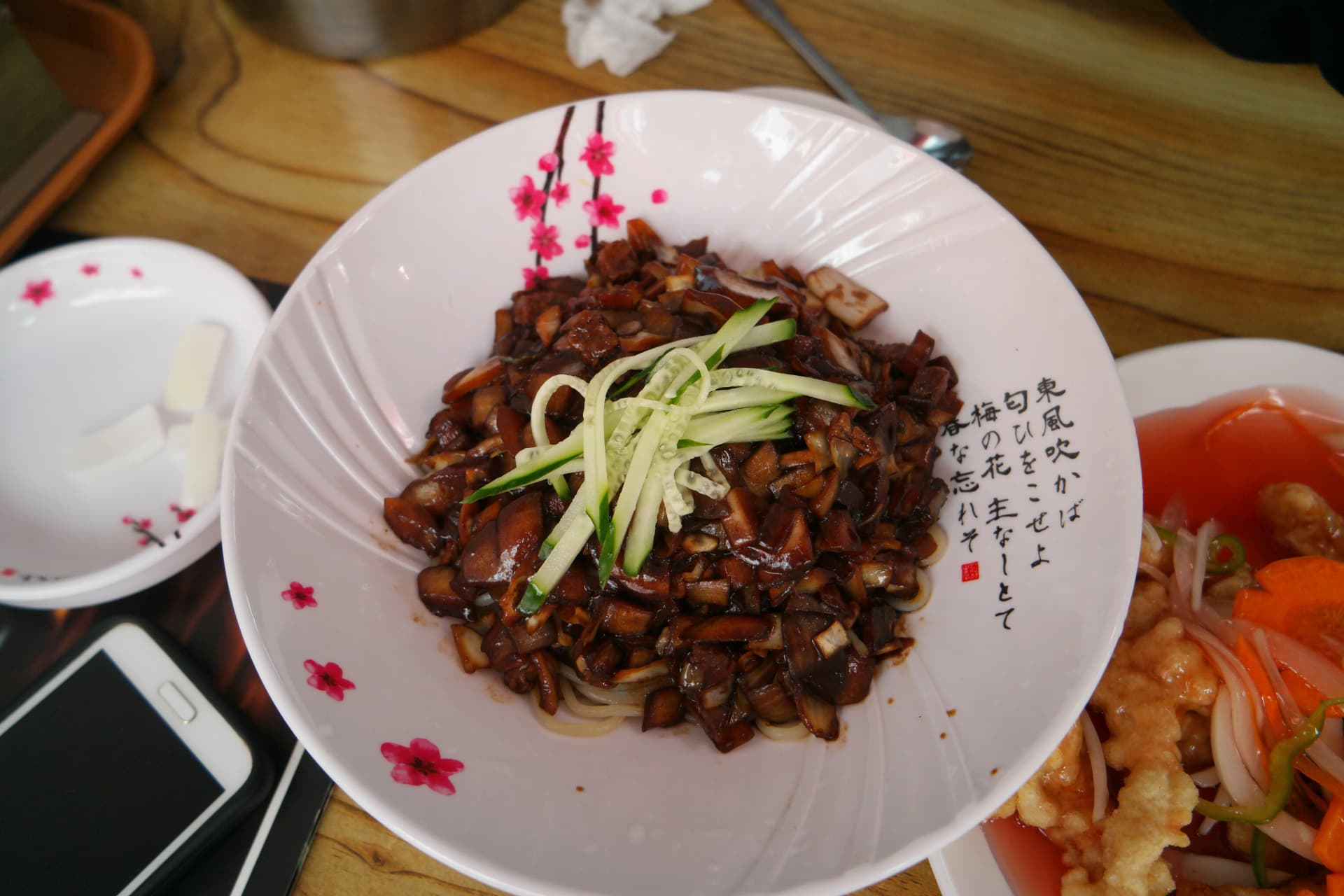 벚꽃 문양 도자기 그릇에 담긴 한국식 짜장면, 새까만 춘장 소스가 면 위를 덮고 채 썬 오이가 올라간 모습 | 하이제이에스비