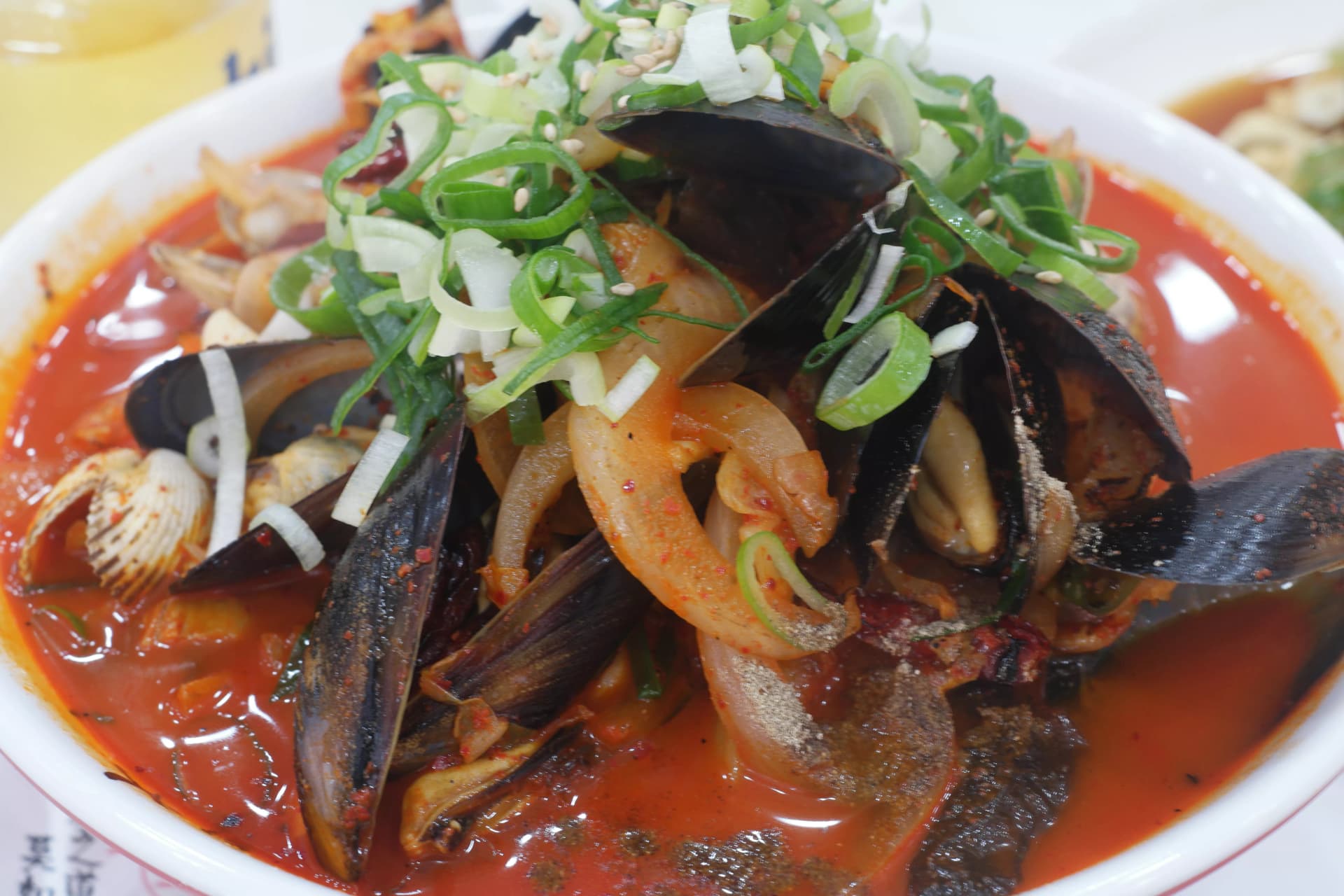 새빨간 국물에 홍합 오징어 바지락이 가득 담긴 한국식 짬뽕, 대파와 깨가 뿌려진 모습 | 하이제이에스비