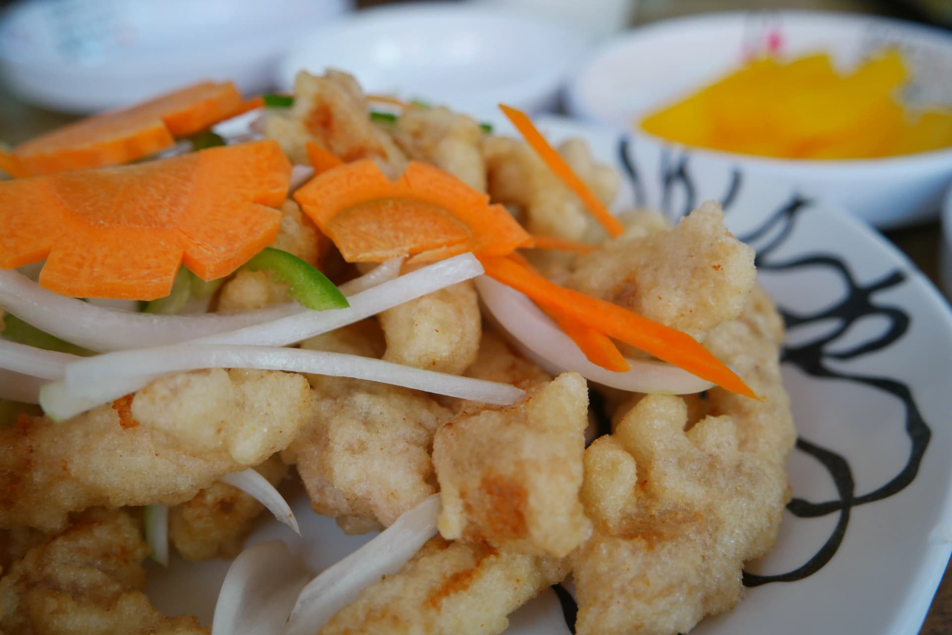 탕수육 개별 튀김 클로즈업, 거칠고 불규칙한 튀김옷 표면과 옆에 놓인 당근 양파가 보이는 모습 | 하이제이에스비