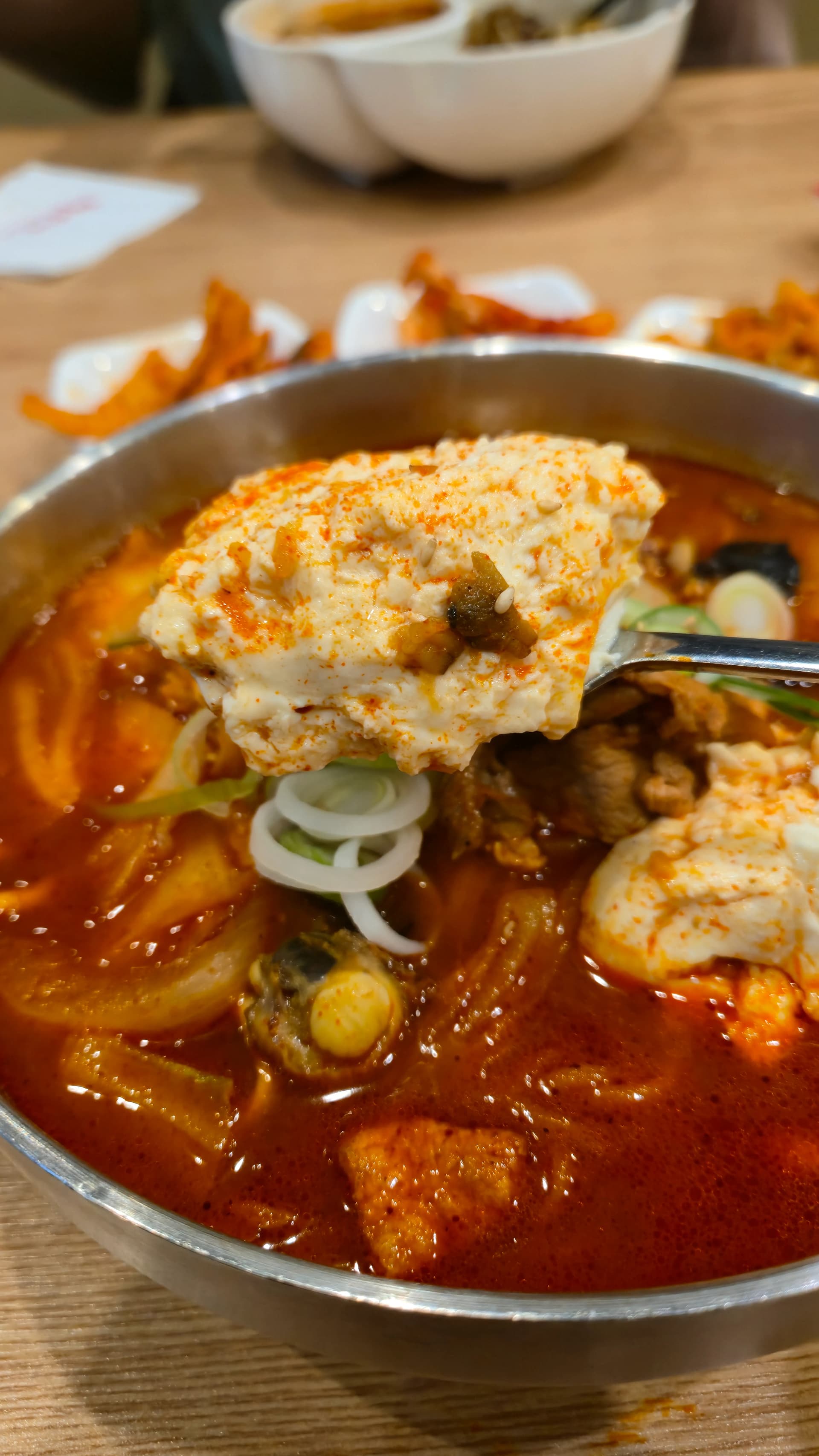 순두부짬뽕에서 숟가락으로 순두부를 떠올린 모습, 부드러운 흰 순두부가 빨간 국물 위에 올라와 있다