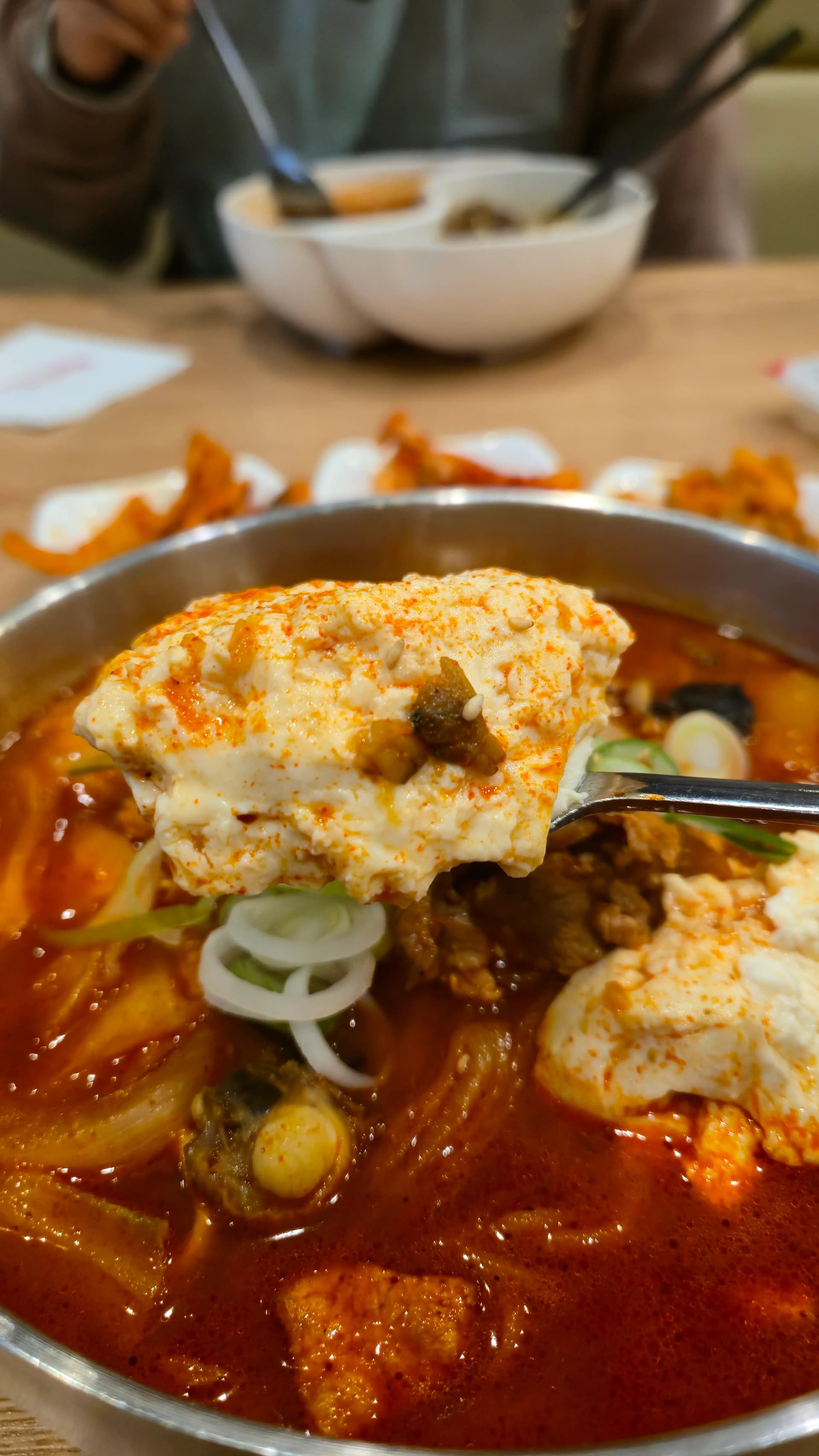 순두부짬뽕 클로즈업, 순두부 덩어리가 빨간 국물에 반쯤 잠겨 있고 대파와 깨가 보인다