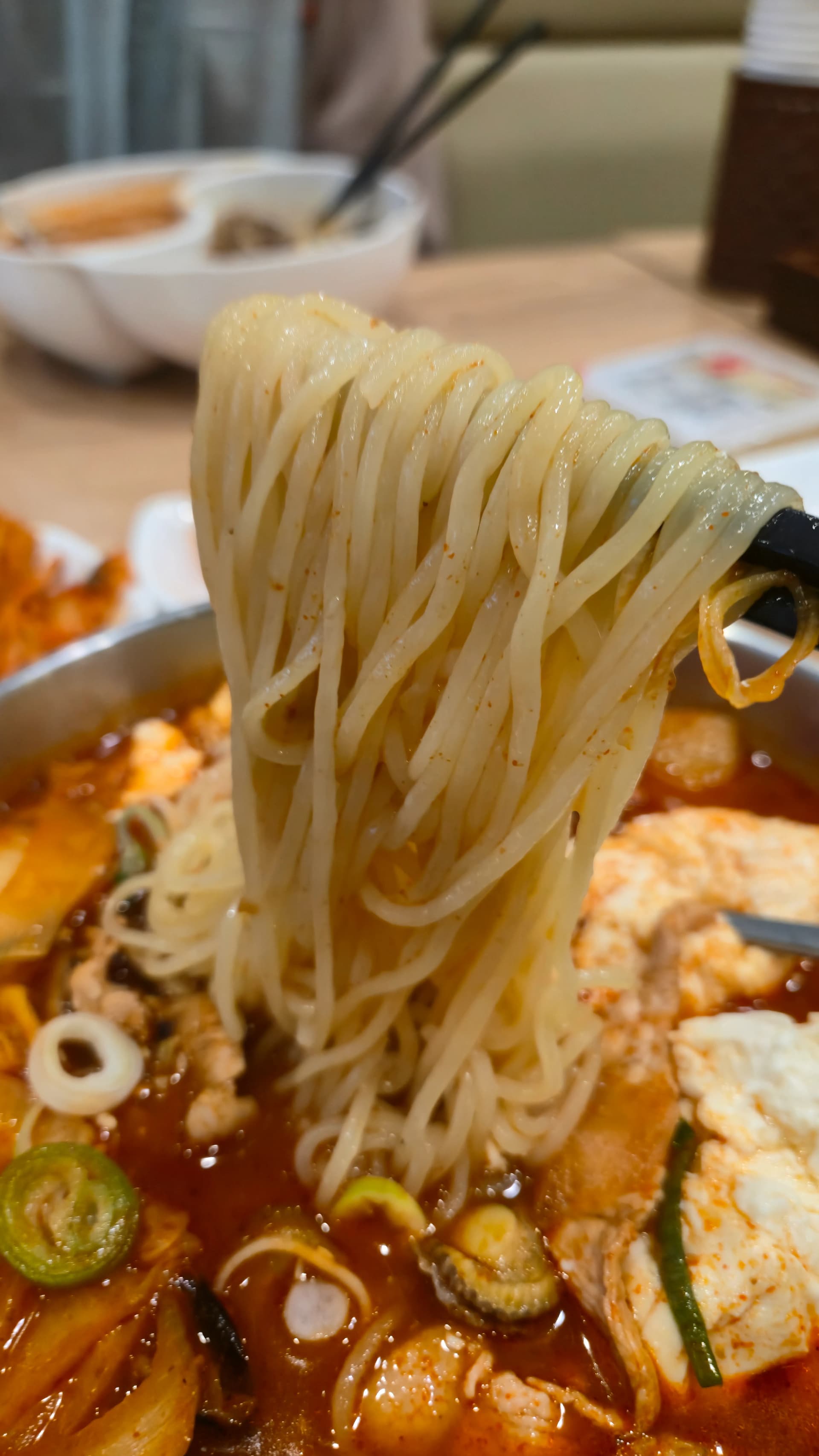젓가락으로 짬뽕지존 면을 높이 들어올린 모습, 일반 짬뽕 면보다 얇은 면에 빨간 국물이 배어 있다