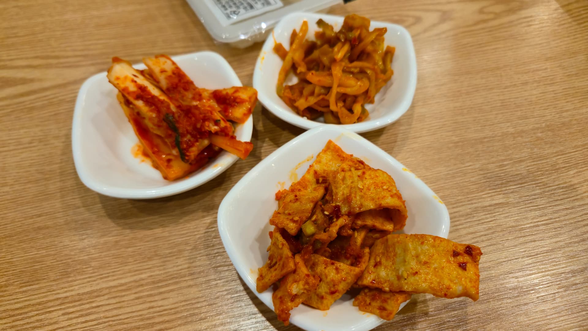 짬뽕지존 테이블 위에 김치 짜사이 어묵무침 세 접시와 개별 포장 단무지가 세팅된 전체 모습