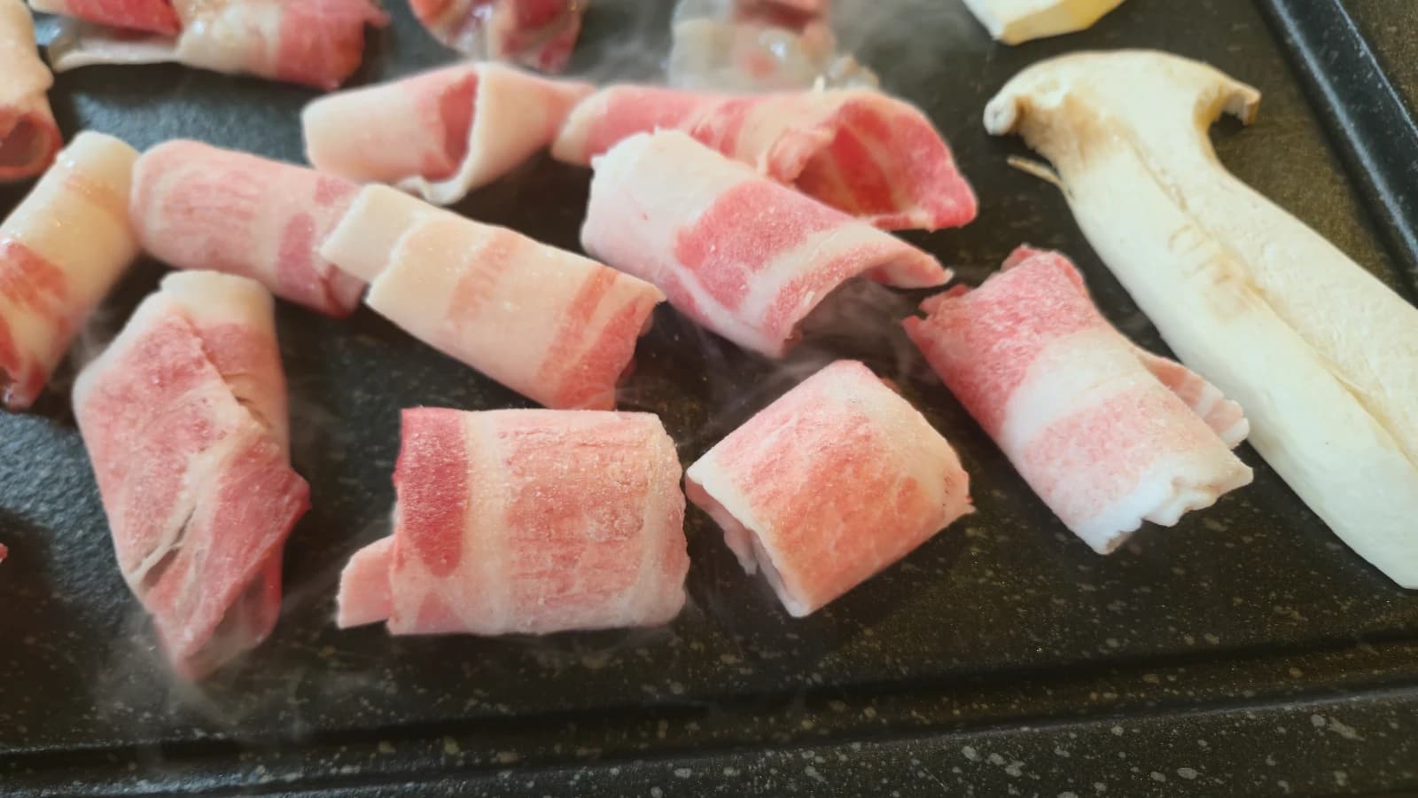 Láminas finas de daepae samgyeopsal y setas de ostra desplegadas en la plancha