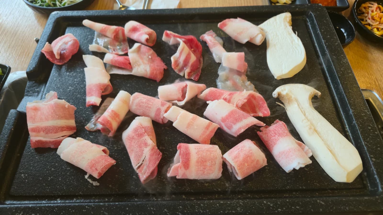 Humo subiendo mientras se asa el daepae samgyeopsal en la plancha