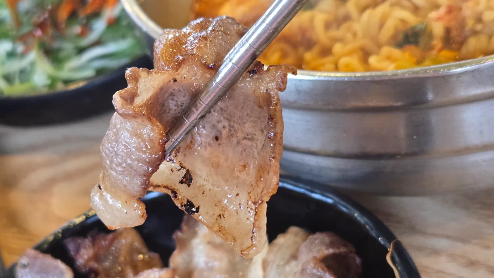 Palitos levantando una lámina brillante de daepae asado con grasa reluciente