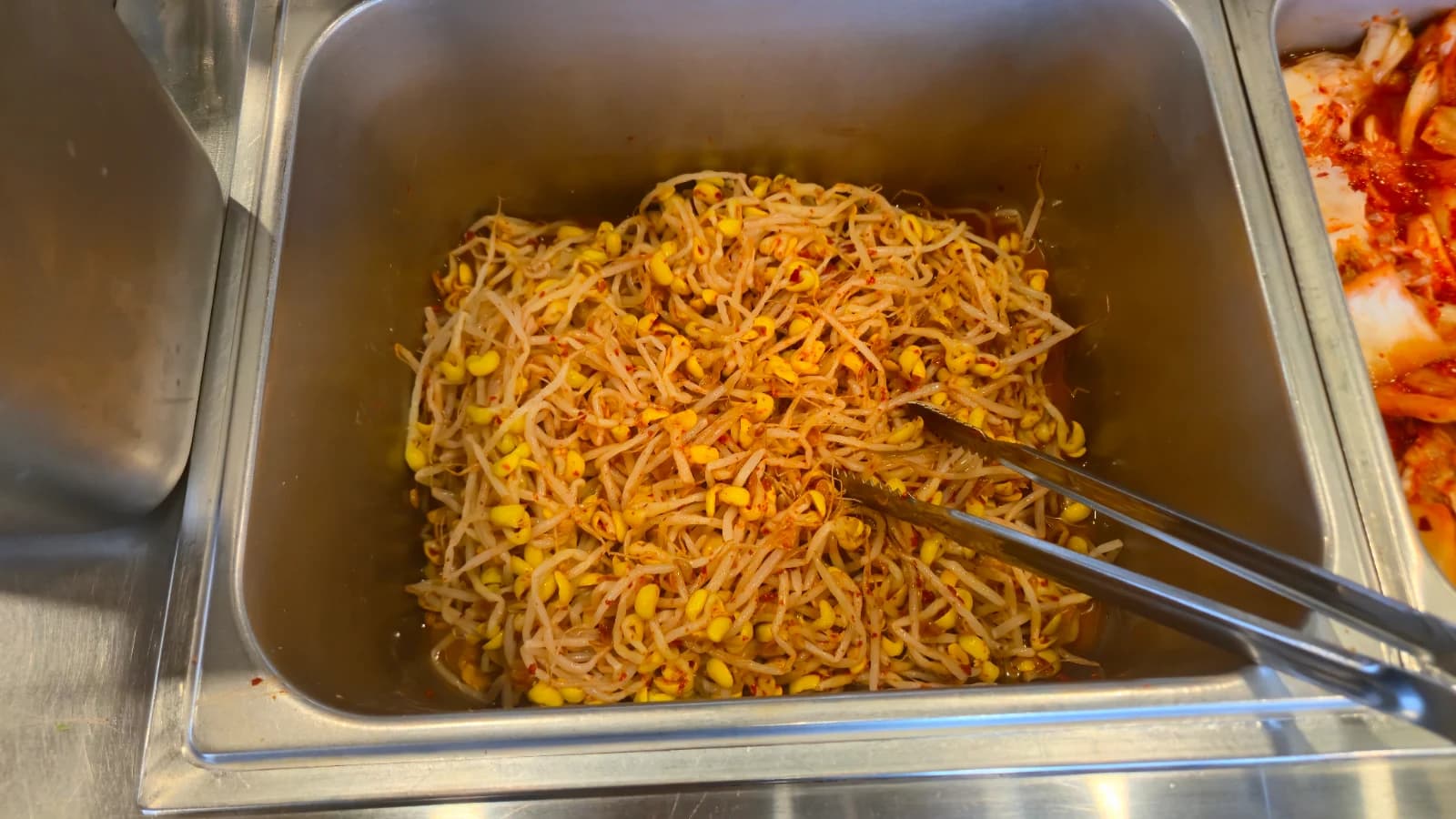 Brotes de soja aliñados en el mesón self-service, sirviéndose con pinzas