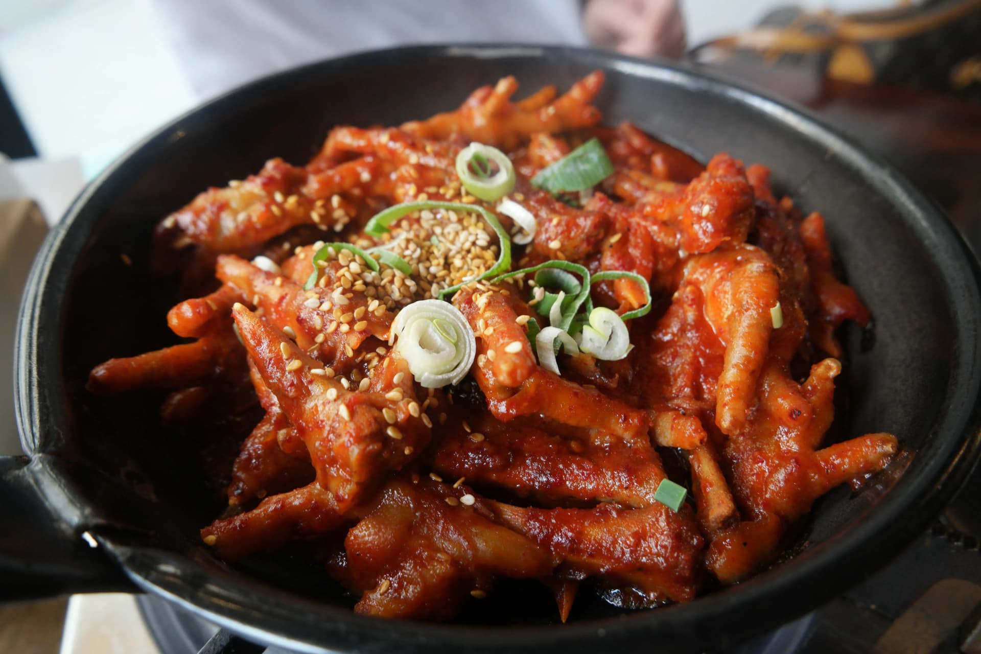 Dakbal con caldo picante de Hanshin Pocha sobre una plancha negra, con patas rojas cubiertas de salsa, ajonjolí y cebolla china encima