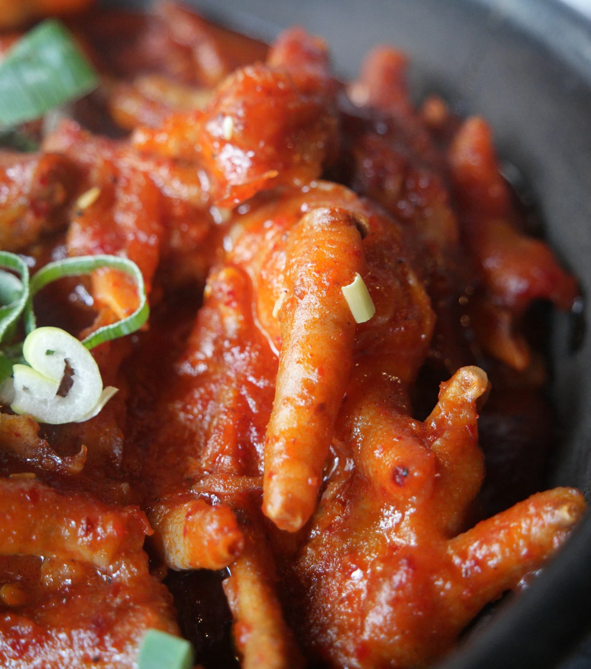 Primer plano de patas de pollo rojas impregnadas de salsa picante, con la forma de los dedos todavía bien visible