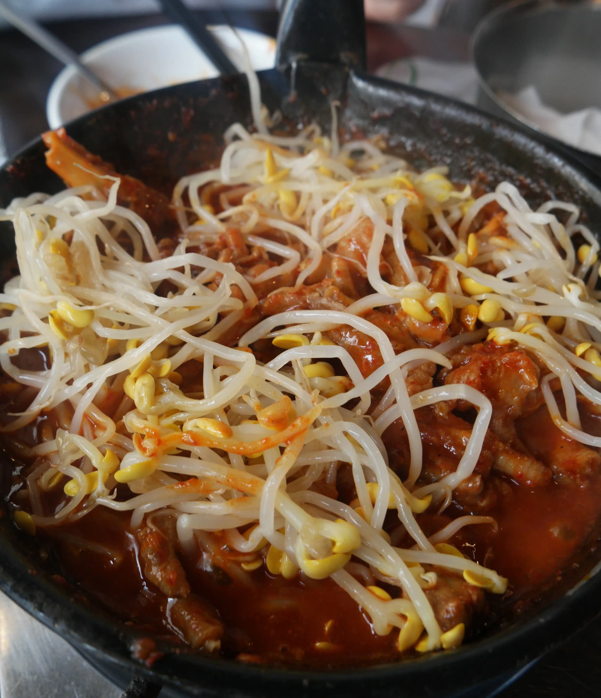 Brotes de soya mezclados con patas de pollo mientras absorben la salsa roja, con contraste entre el blanco y el rojo