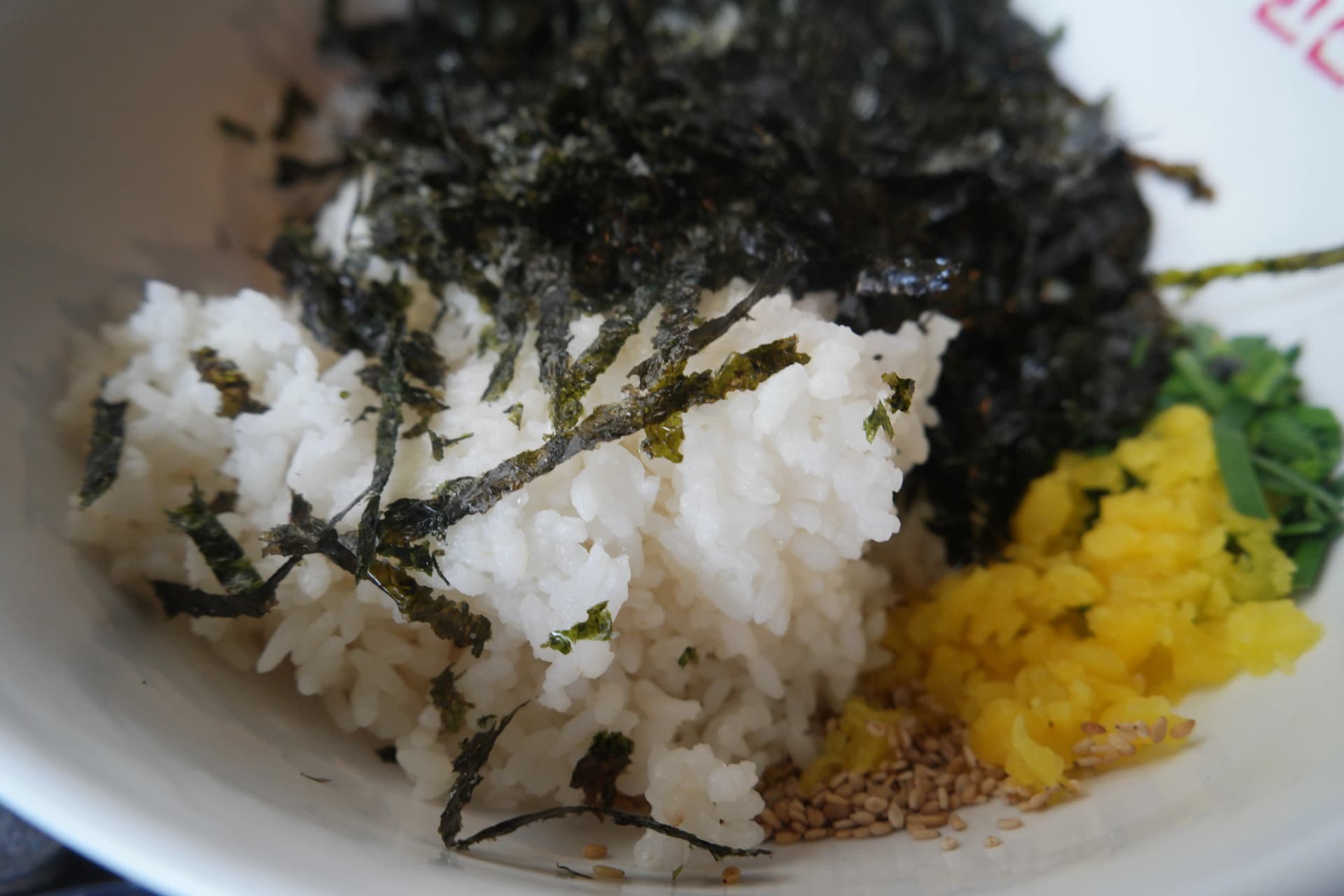 Primer plano de arroz con hojuelas de alga, rabanito amarillo encurtido y ajonjolí para preparar jumokbap