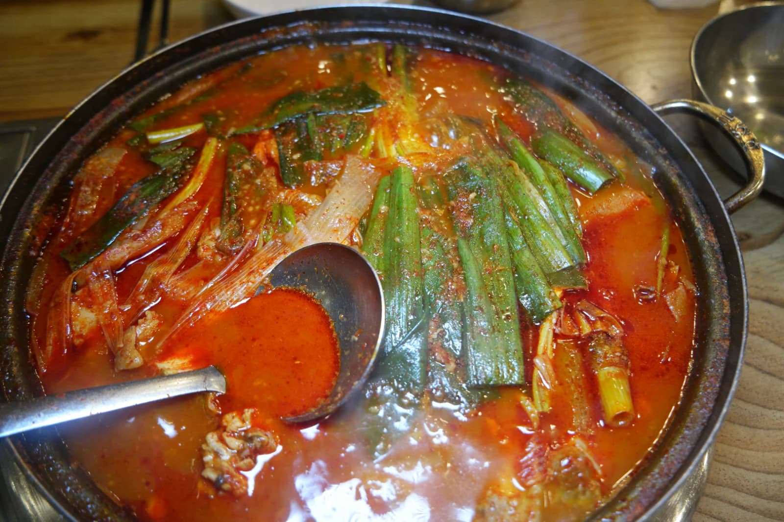 Full pot of dakbokkeumtang with red spicy broth, long scallion pieces on top, and chicken and potatoes submerged below